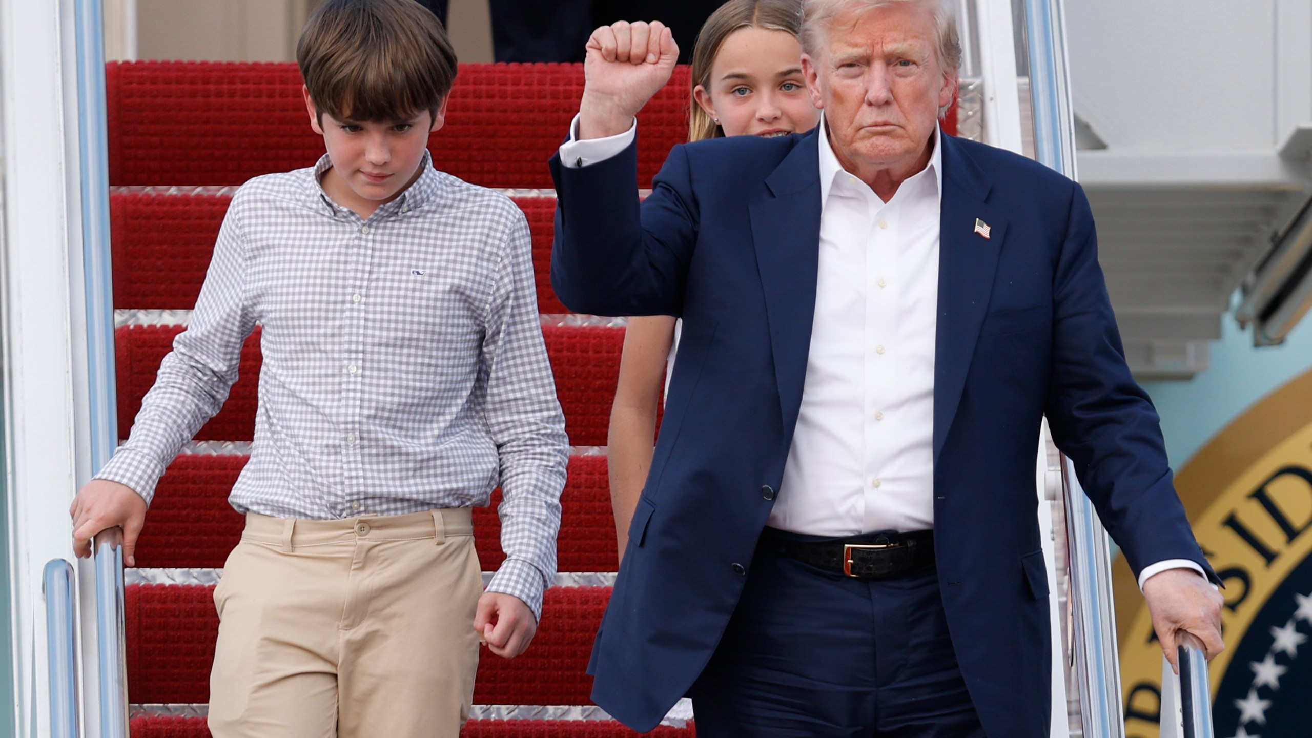 President Donald Trump, front right, gestures as he walks down the stairs of Air Force One with his grandchildren, Spencer, left, and Chloe, back center, upon his arrival at Joint Base Andrews, Md., Tuesday, July 29, 2025. (AP Photo/Luis M. Alvarez)