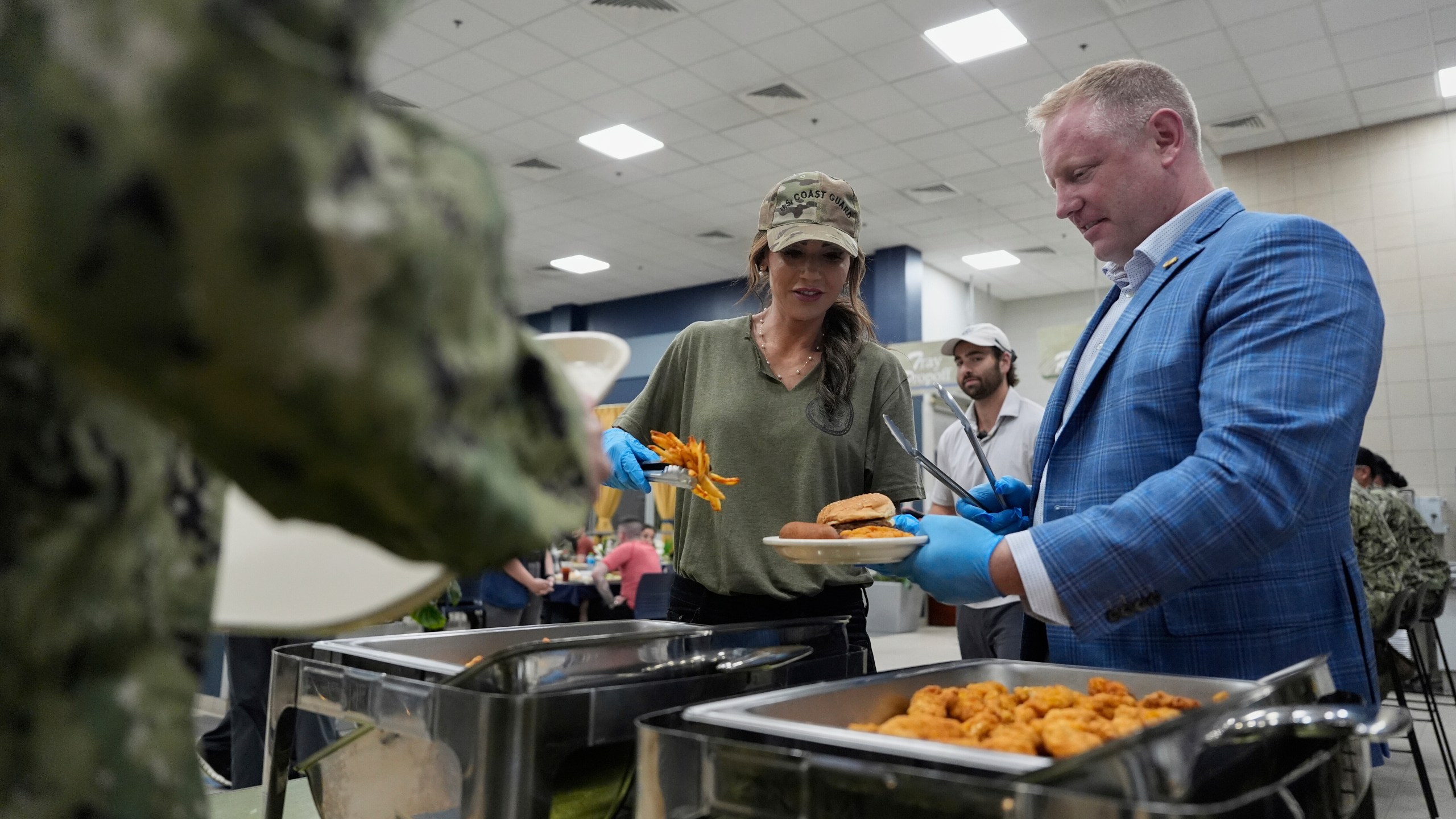 FILE - Homeland Security Secretary Kristi Noem and Sean Plankey, Senior adviser to the Secretary for the U.S. Coast Guard, right, help serve sailors and Coast Guardsmen at Naval Support Activity in Bahrain, May 24, 2025. (AP Photo/Alex Brandon, Pool, File)
