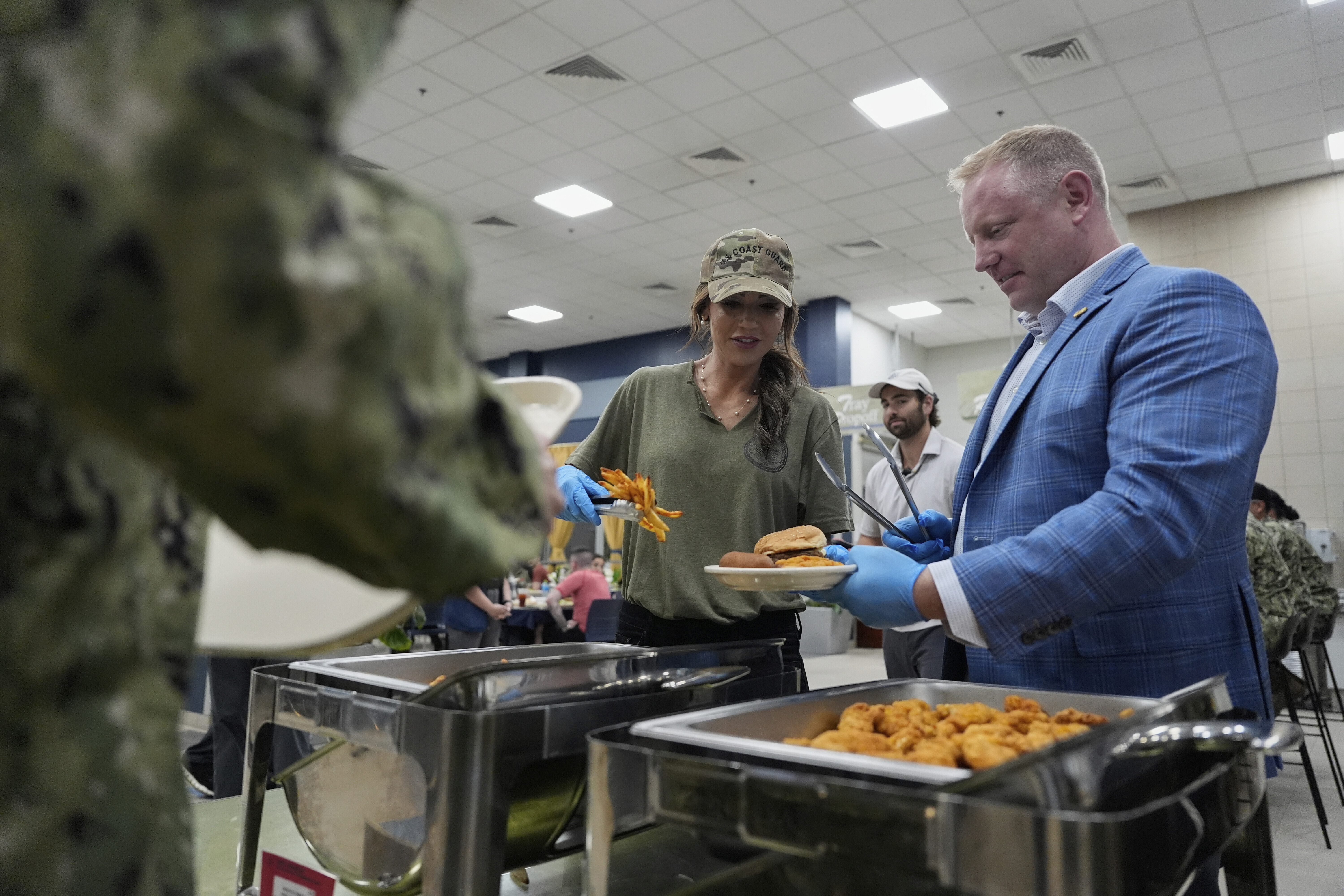 FILE - Homeland Security Secretary Kristi Noem and Sean Plankey, Senior adviser to the Secretary for the U.S. Coast Guard, right, help serve sailors and Coast Guardsmen at Naval Support Activity in Bahrain, May 24, 2025. (AP Photo/Alex Brandon, Pool, File)