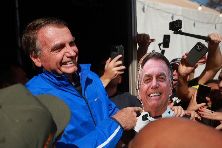 Brazil's former President Jair Bolsonaro points a photo of him during a motorcycle caravan by supporters to protest the Supreme Court trial where he faces charges for alleged involvement in a 2022 coup attempt, in Brasília, Brazil, Tuesday, July 29, 2025. (AP Photo/Luis Nova)