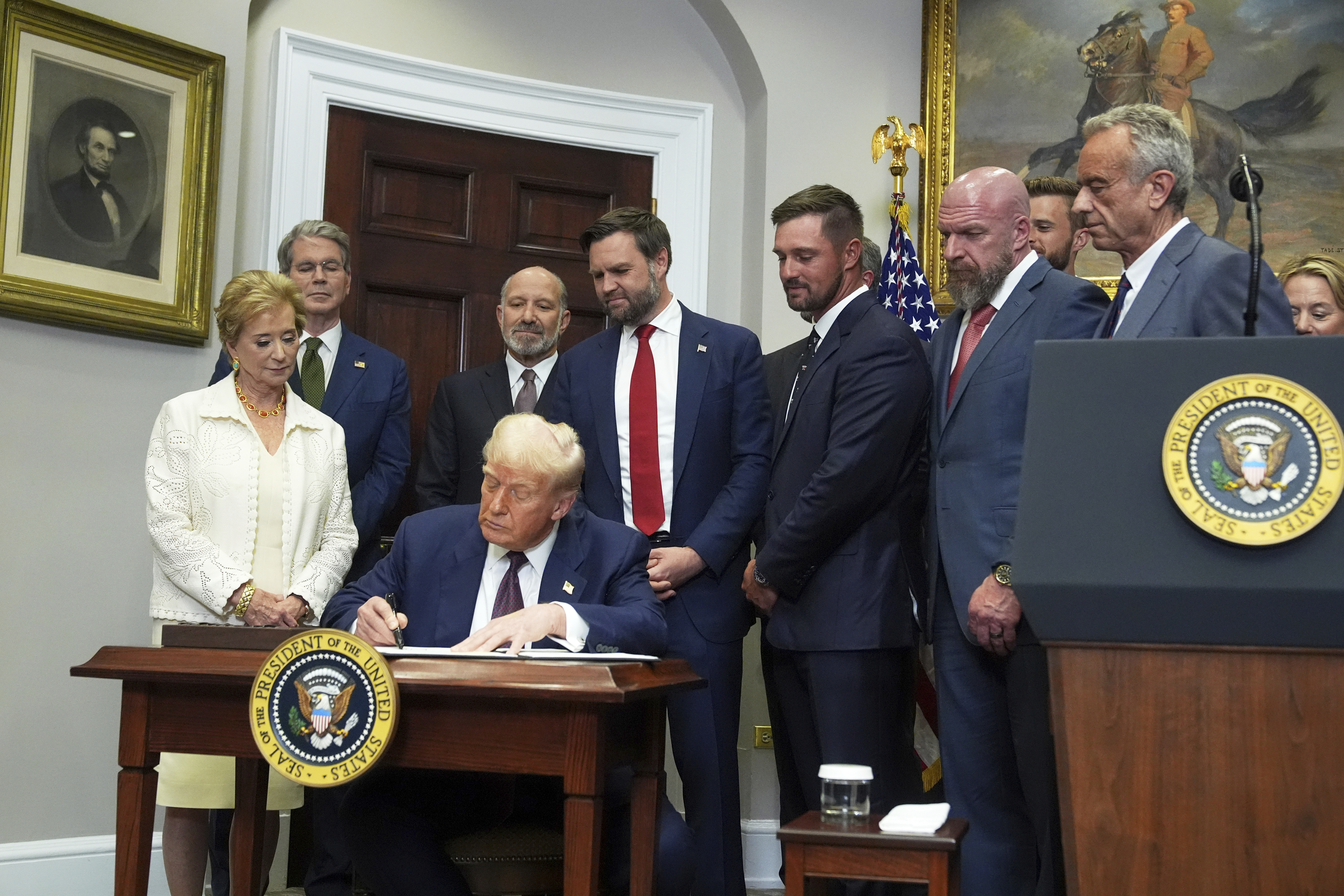 President Donald Trump signs an executive order restarting the Presidential Fitness Test in public schools as Secretary of Education Linda McMahon, from left, Treasury Secretary Scott Bessent, Commerce Secretary Howard Lutnick, Vice President JD Vance, professional golfer Bryson DeChambeau, WWE CCO Triple H and Health and Human Services Secretary Robert F. Kennedy Jr. watch, Thursday, July 31, 2025, in the Roosevelt Room of the White House in Washington. (AP Photo/Jacquelyn Martin)