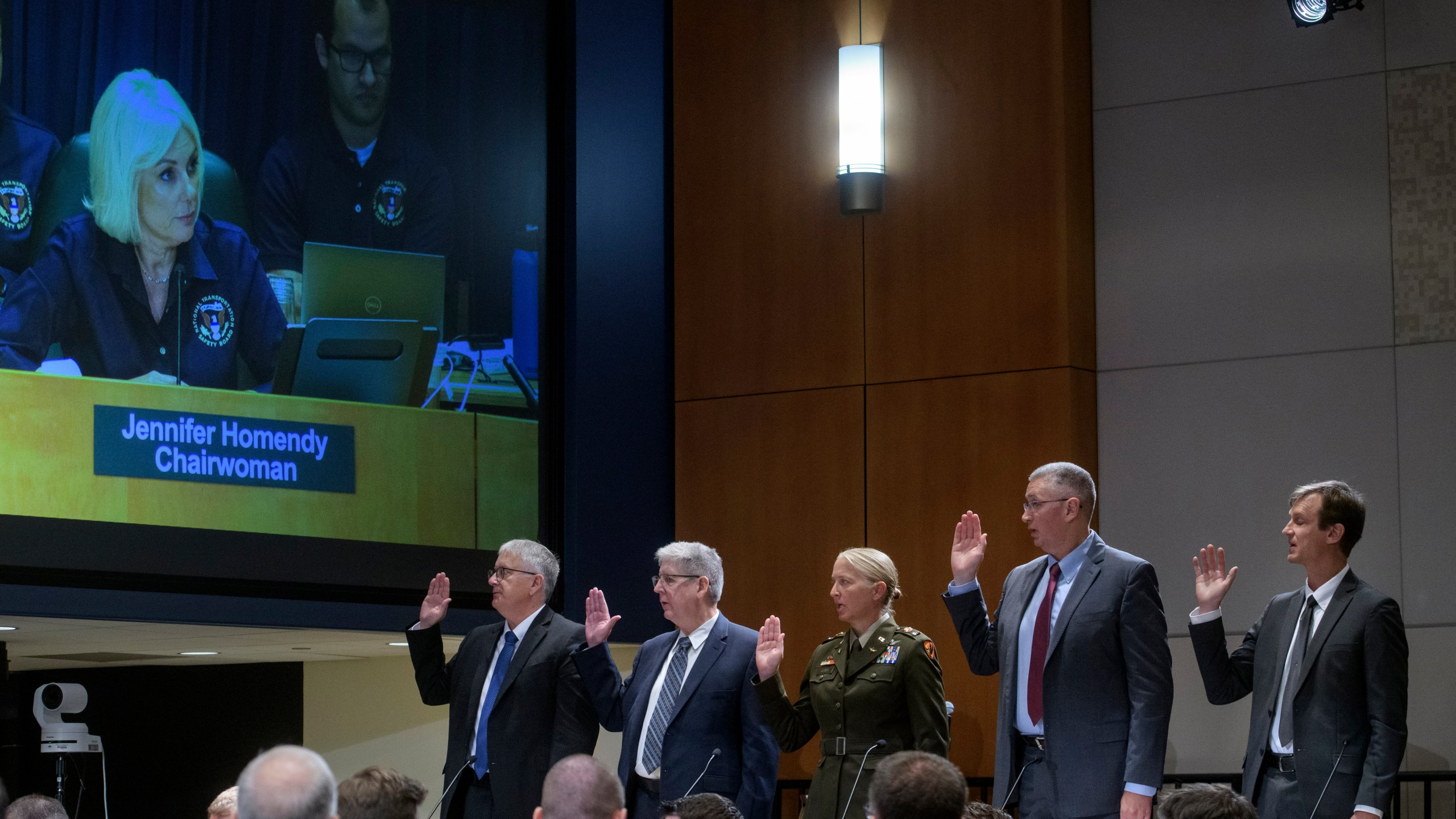 National Transportation Safety Board Chairwoman Jennifer Homendy, on monitor left, swears-in the witnesses from left: Dan Cooper, Sikorsky Aircraft, Lance Gant, Federal Aviation Administration, U.S. Army CW4 Kylene Lewis, Steve Braddom, U.S. Army, and Scott Rosengren, U.S. Army, during the NTSB fact-finding hearing on the DCA midair collision accident, at the National Transportation and Safety Board boardroom, Wednesday, July 30, 2025, in Washington. (AP Photo/Rod Lamkey, Jr.)