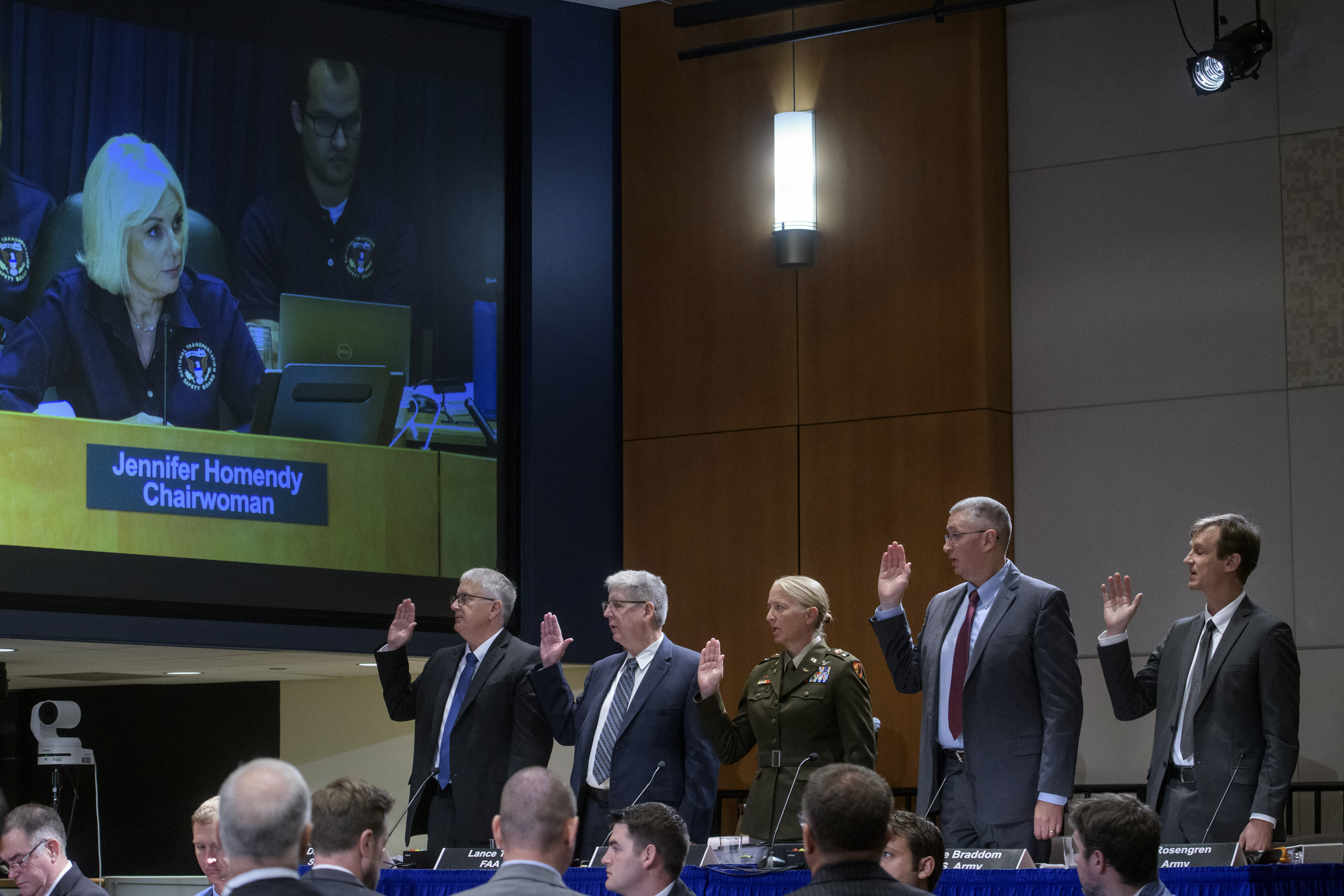 National Transportation Safety Board Chairwoman Jennifer Homendy, on monitor left, swears-in the witnesses from left: Dan Cooper, Sikorsky Aircraft, Lance Gant, Federal Aviation Administration, U.S. Army CW4 Kylene Lewis, Steve Braddom, U.S. Army, and Scott Rosengren, U.S. Army, during the NTSB fact-finding hearing on the DCA midair collision accident, at the National Transportation and Safety Board boardroom, Wednesday, July 30, 2025, in Washington. (AP Photo/Rod Lamkey, Jr.)