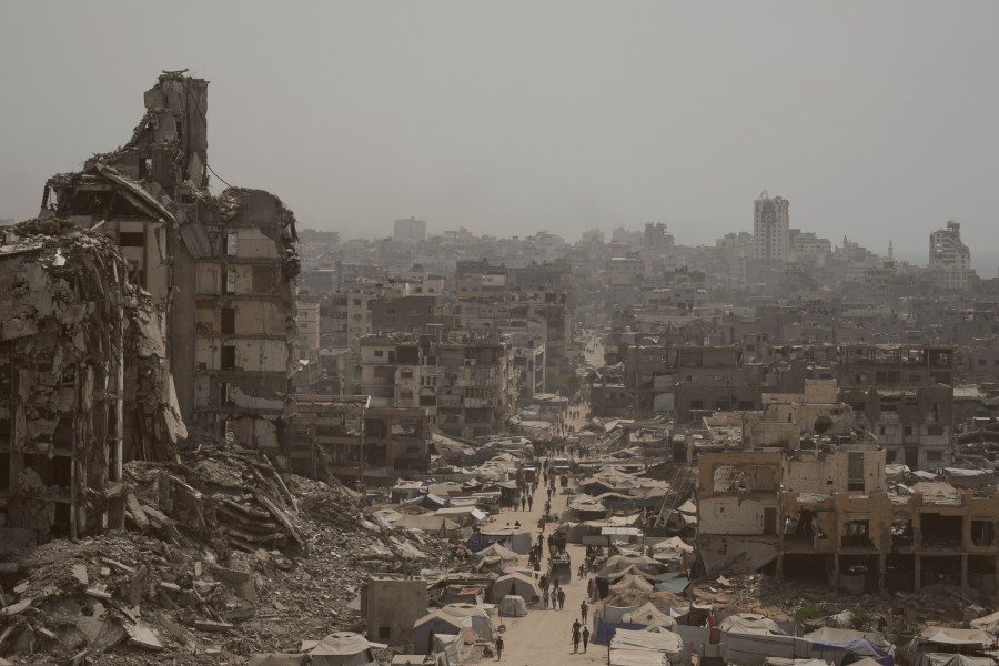 People walk along a street lined with destroyed buildings following Israeli bombardments during the Israel-Hamas war in the Gaza Strip, Tuesday, July 29, 2025. (AP Photo/Jehad Alshrafi)