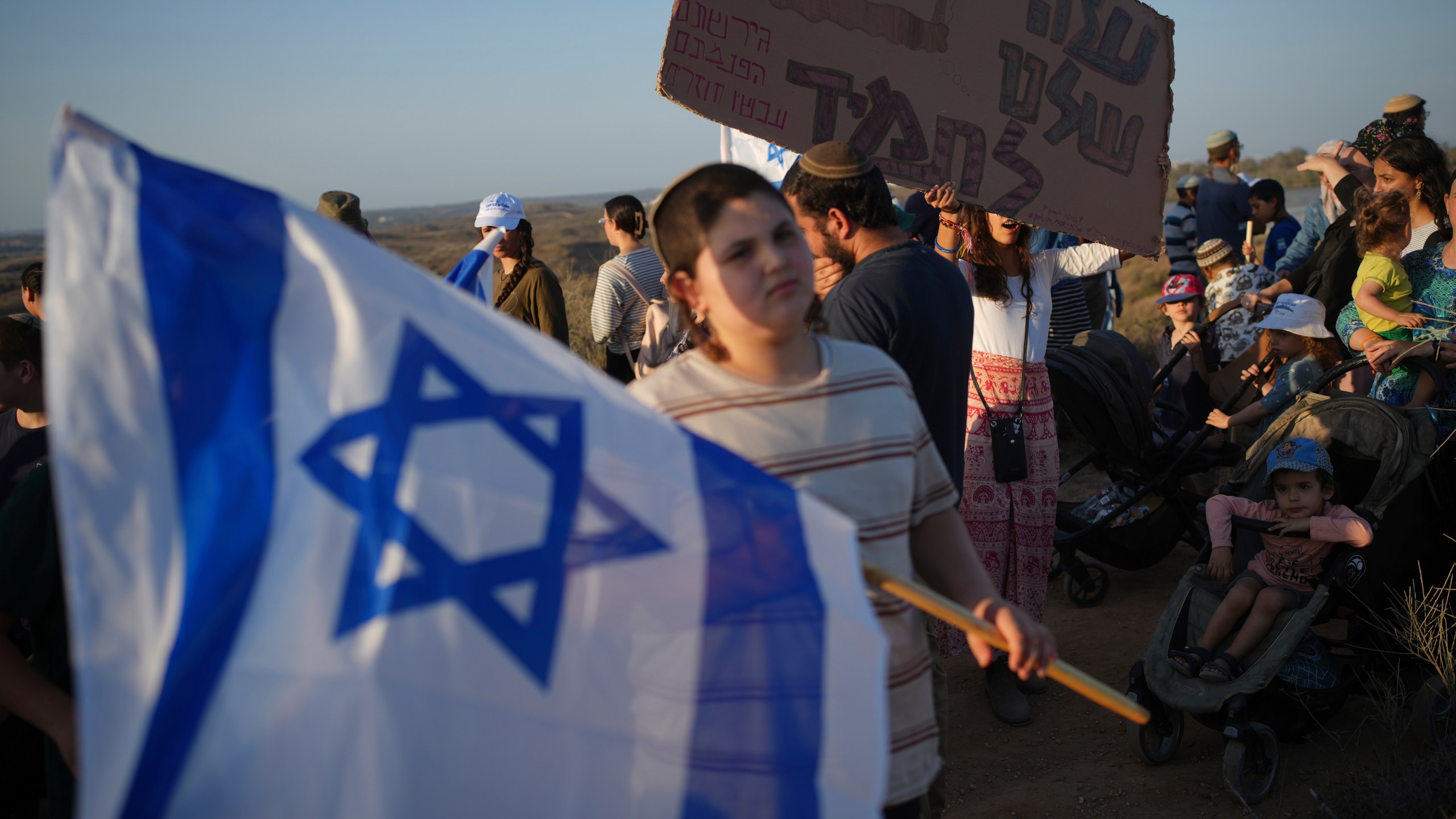 Israeli right-wing activists, one holding a sign ""Gaza is ours forever," attend a rally calling for the re-establishment of Jewish settlements in the Gaza Strip, near the border in southern Israel, Wednesday, July 30, 2025. (AP Photo/Ohad Zwigenberg)