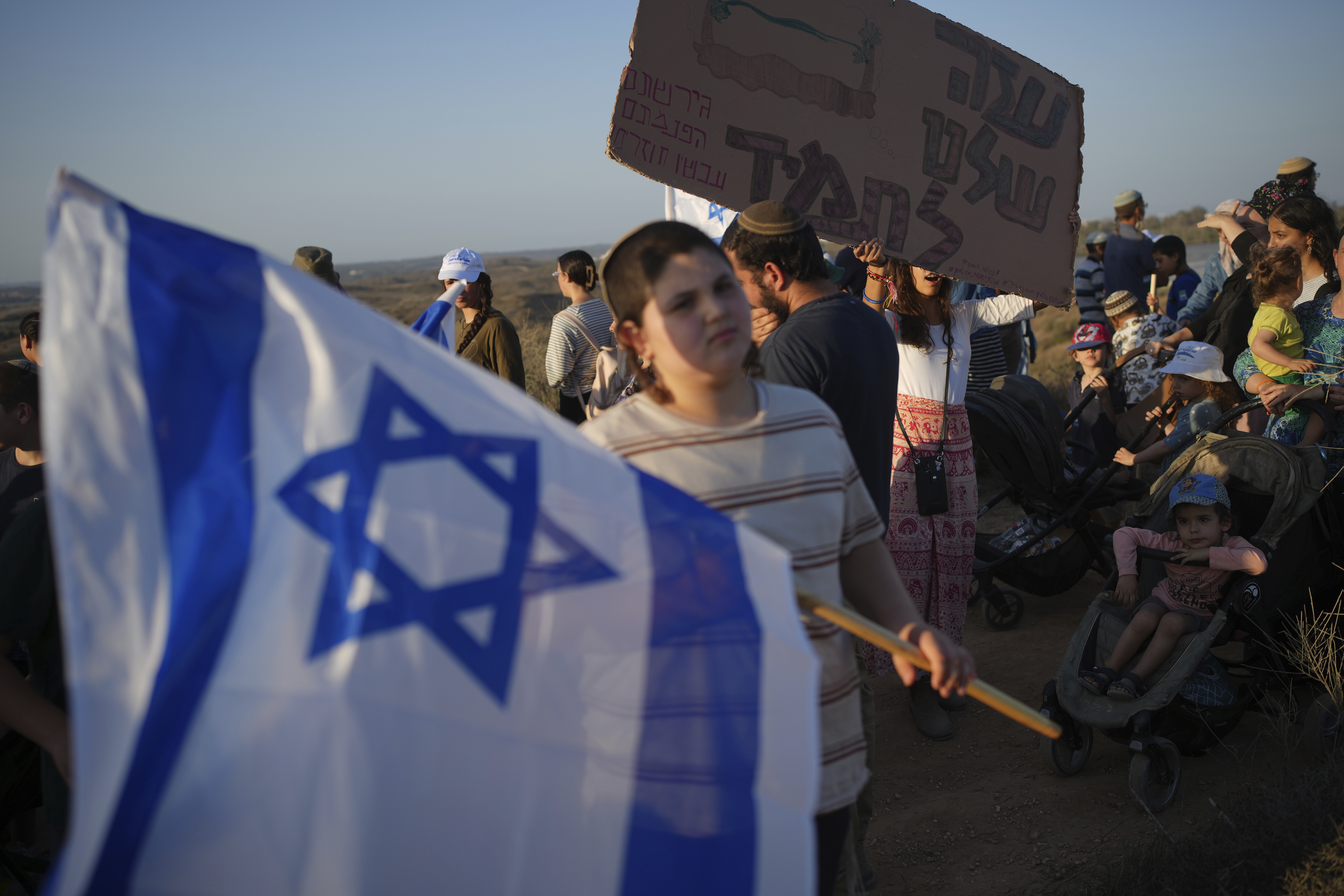 Israeli right-wing activists, one holding a sign ""Gaza is ours forever," attend a rally calling for the re-establishment of Jewish settlements in the Gaza Strip, near the border in southern Israel, Wednesday, July 30, 2025. (AP Photo/Ohad Zwigenberg)
