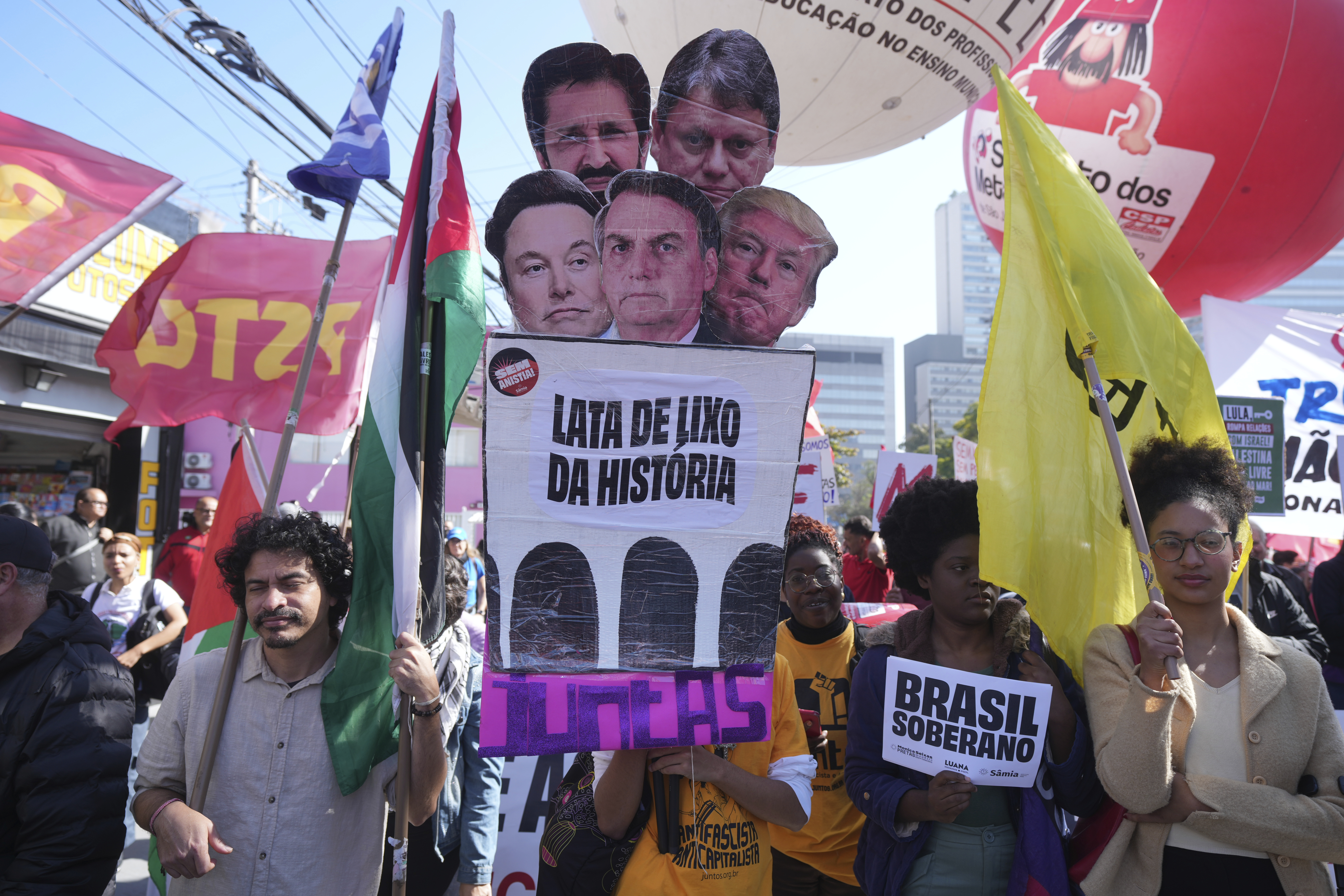 Demonstrators carry a sign that reads in Portuguese "The trash can of history, together" and photos of U.S. President Donald Trump, Elon Musk, Sao Paulo's Governor Tarcisio de Freitas, Sao Paulo's Mayor Ricardo Nunes and Brazil's former President Jair Bolsonaro during a protest against a 50% U.S. tariff on Brazilian goods outside the U.S. consulate in Sao Paulo, Friday, Aug. 1, 2025. (AP Photo/Andre Penner)