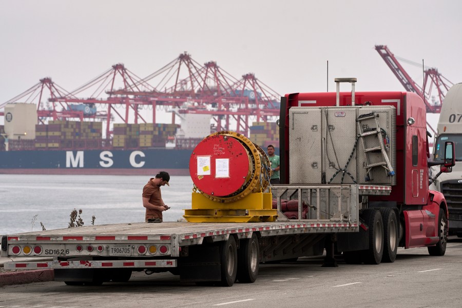 A truck driver secures a heavy machinery prior to transporting it at the Port of Long Beach, Calif., Friday, Aug. 1, 2025. (AP Photo/Damian Dovarganes)