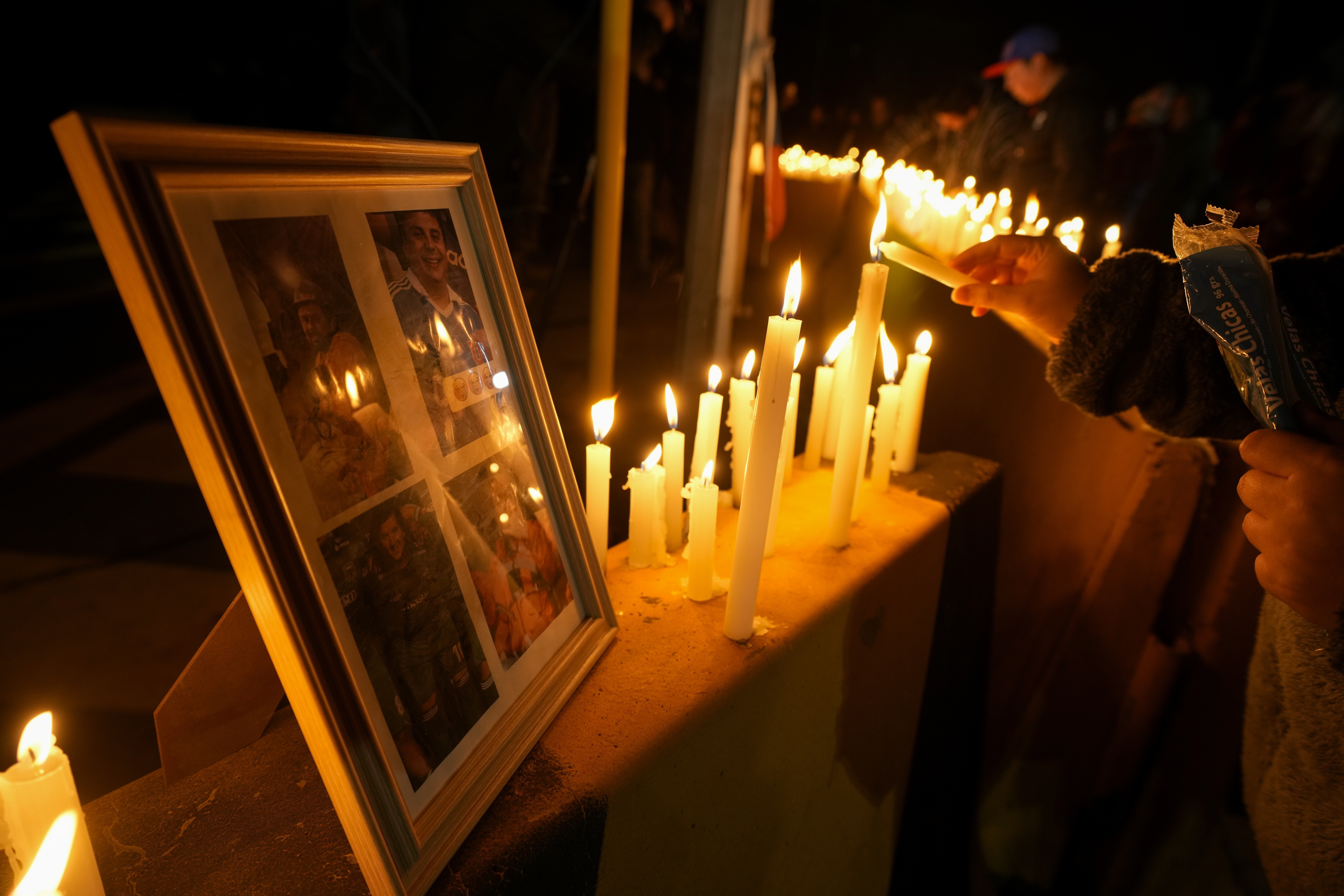 A person lights a candle during a vigil in front of El Teniente copper mine, operated by Codelco, where a cave-in killed one worker and trapped five others underground, halting operations in Rancagua, Chile, Saturday, Aug. 2, 2025. (AP Photo/Esteban Felix)