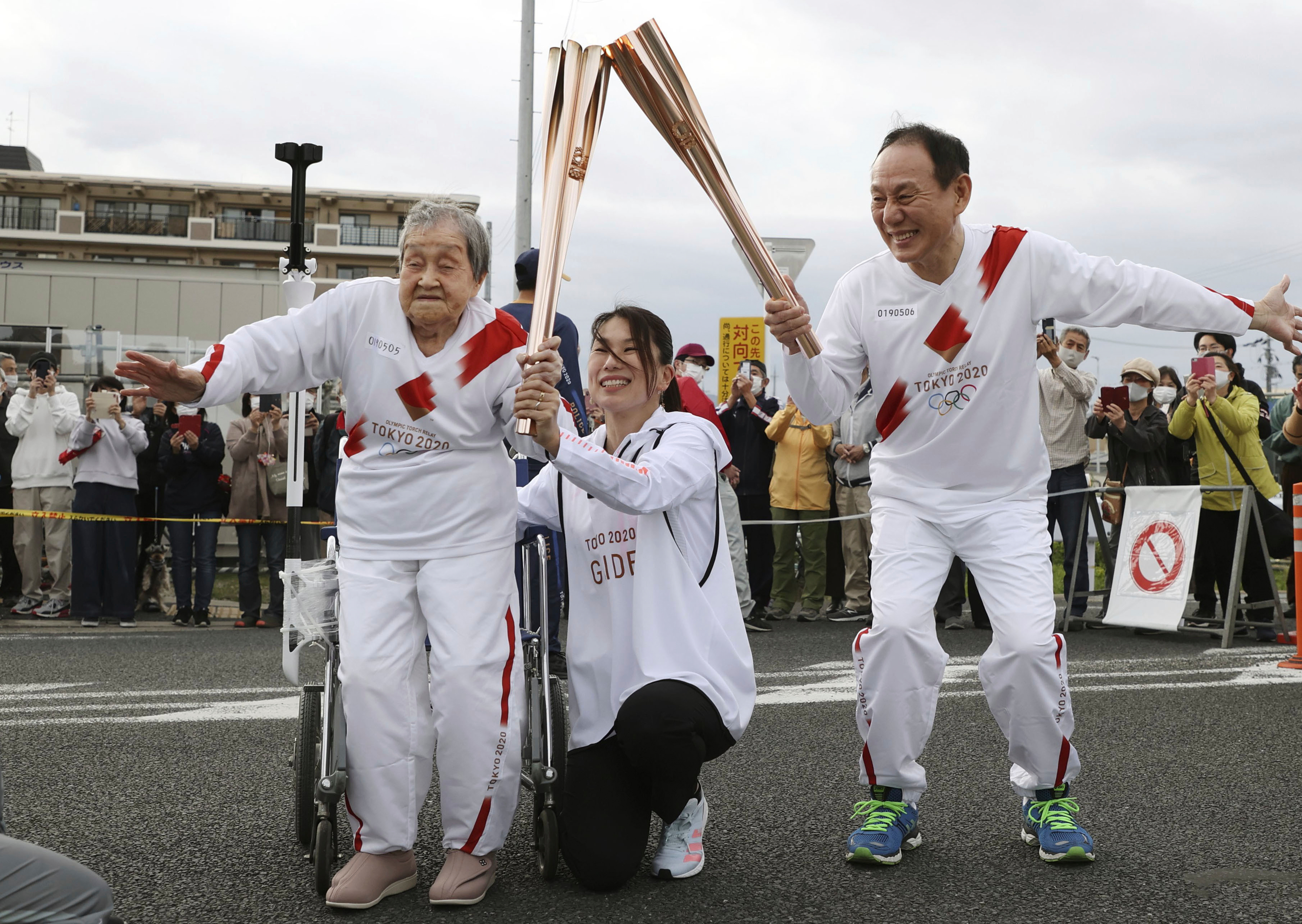 Torchbearer Shigeko Kagawa, left, hands over the flame of the torch to the next runner during a torch relay event for the Tokyo Olympics in Yamatokooriyama, Nara prefecture, western Japan, April 12, 2021. (Kyodo News via AP)