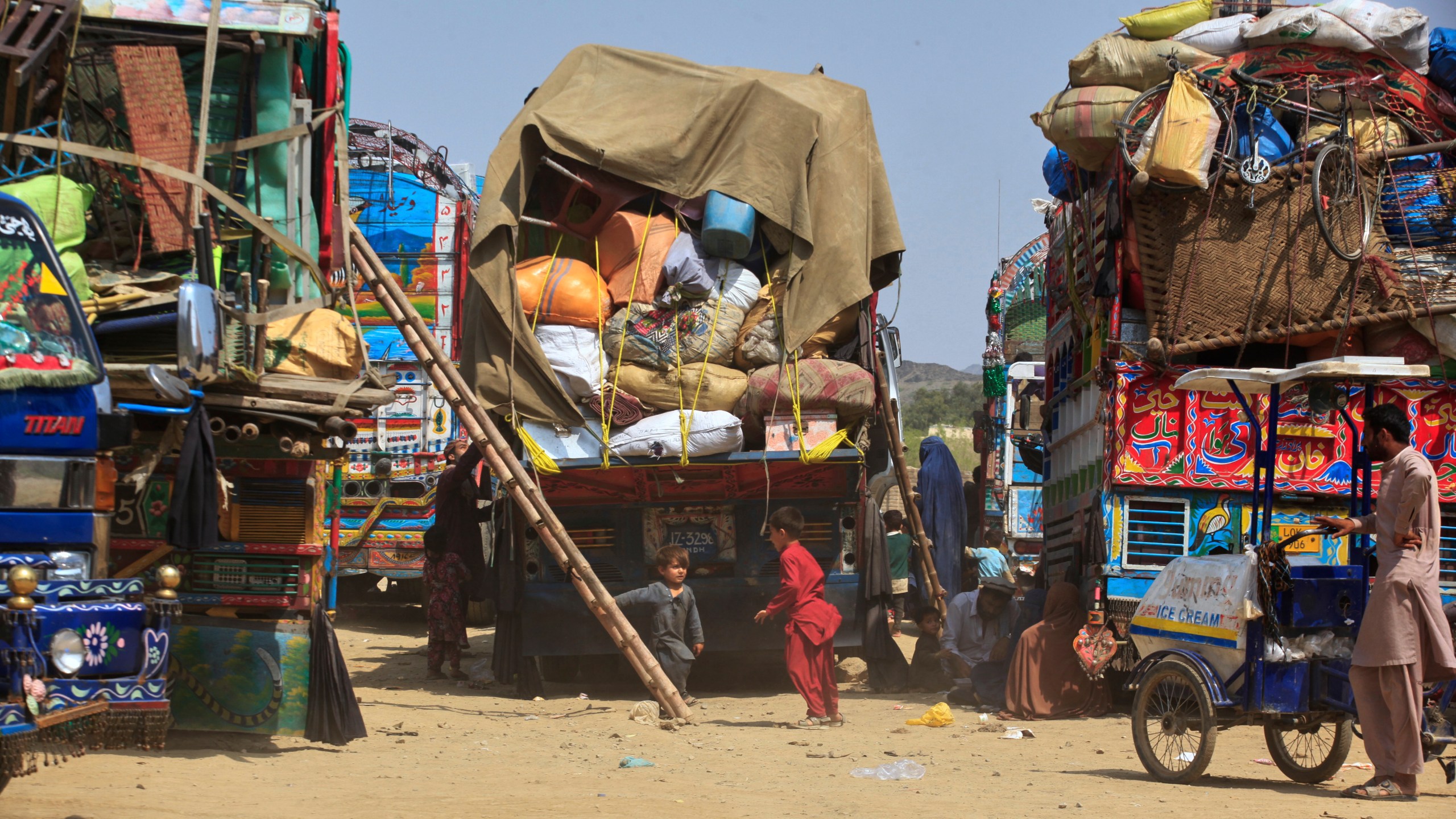 FILE - Afghan refugee children play next to trucks loaded with their family's belongings as they wait to return Afghanistan along a highway in Landi Kotal, Pakistan, April 9, 2025. (AP Photo/Muhammad Sajjad, File)