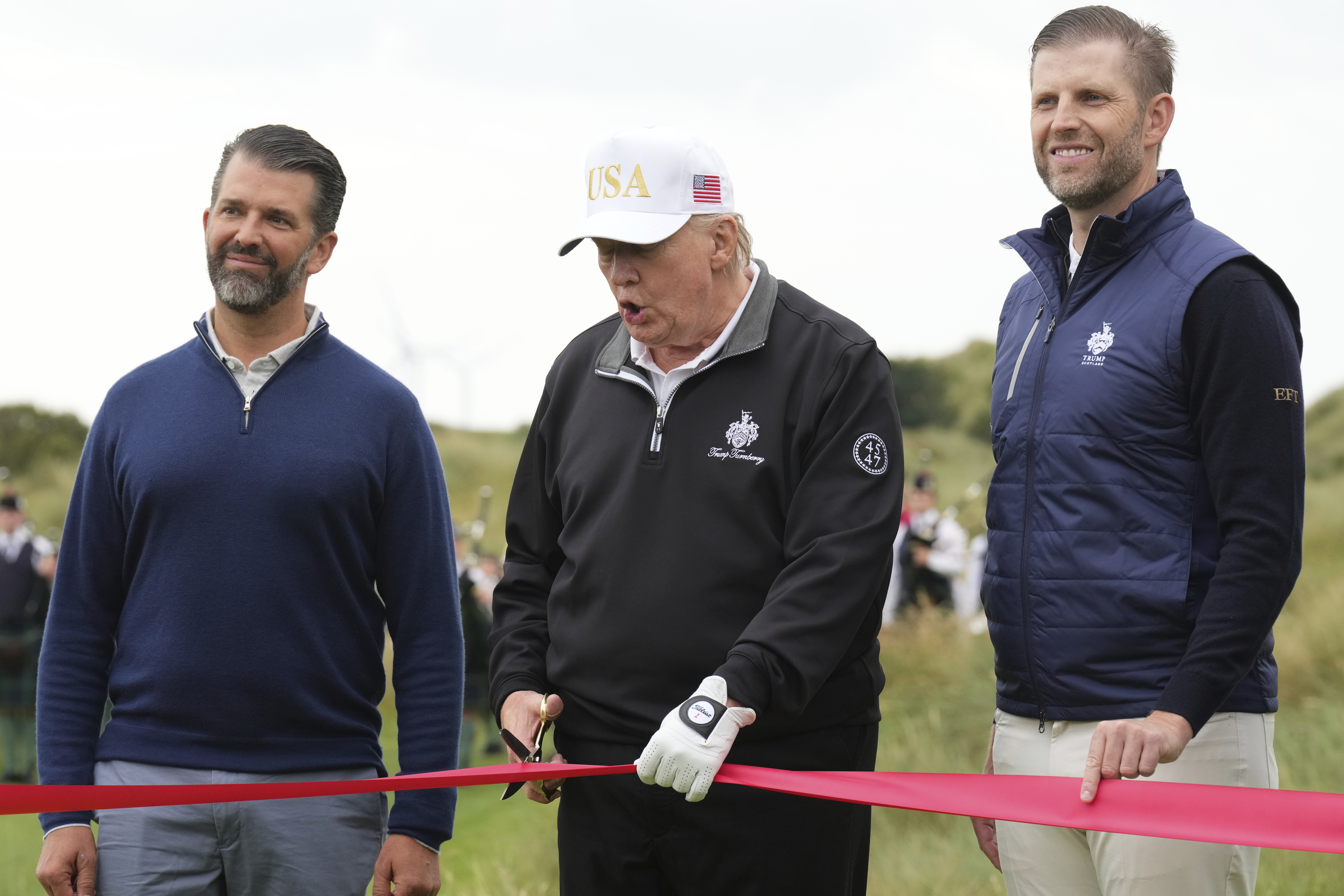 President Donald Trump cuts the ribbon, standing between Donald Trump Jr., left, and Eric Trump, during an opening ceremony for the Trump International Golf Links golf course, near Aberdeen, Scotland, Tuesday, July 29, 2025. (AP Photo/Jacquelyn Martin)