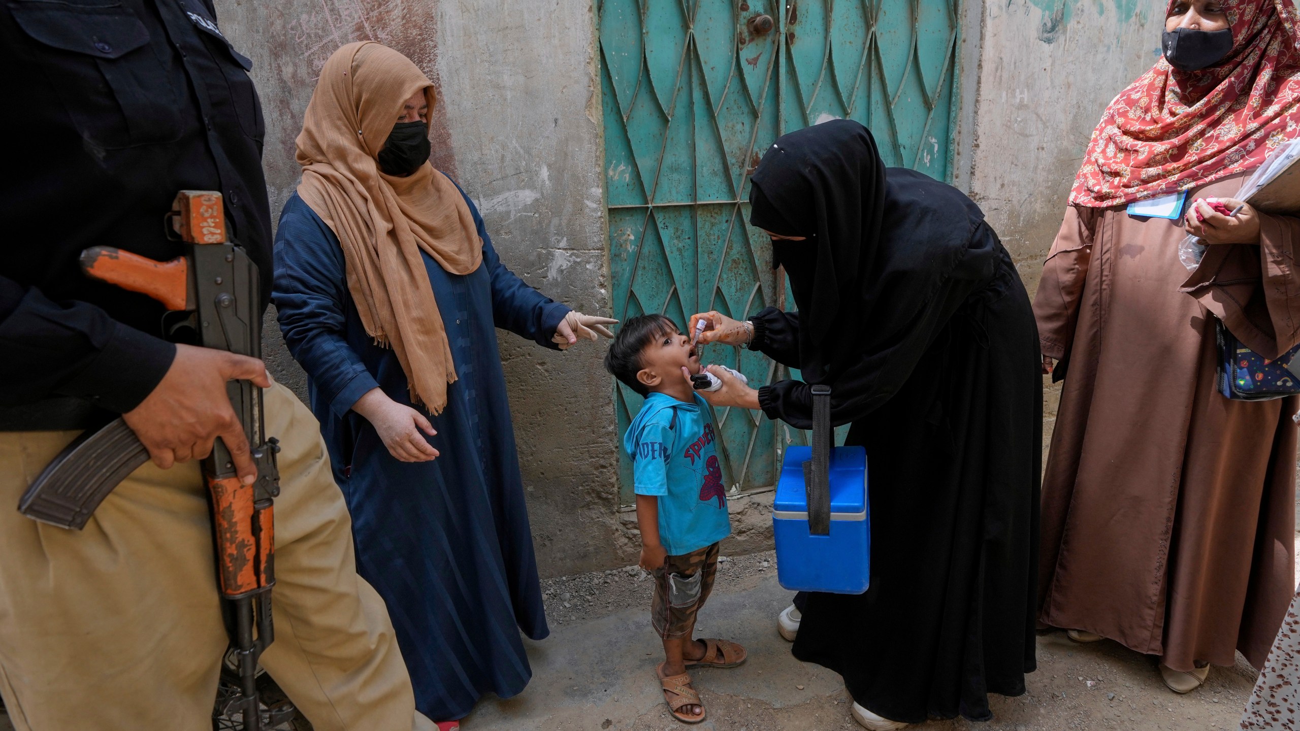 A police officer stands guard while a health worker, center, administers a polio vaccine to a child in Karachi, Pakistan, April 21, 2025. (AP Photo/Fareed Khan)