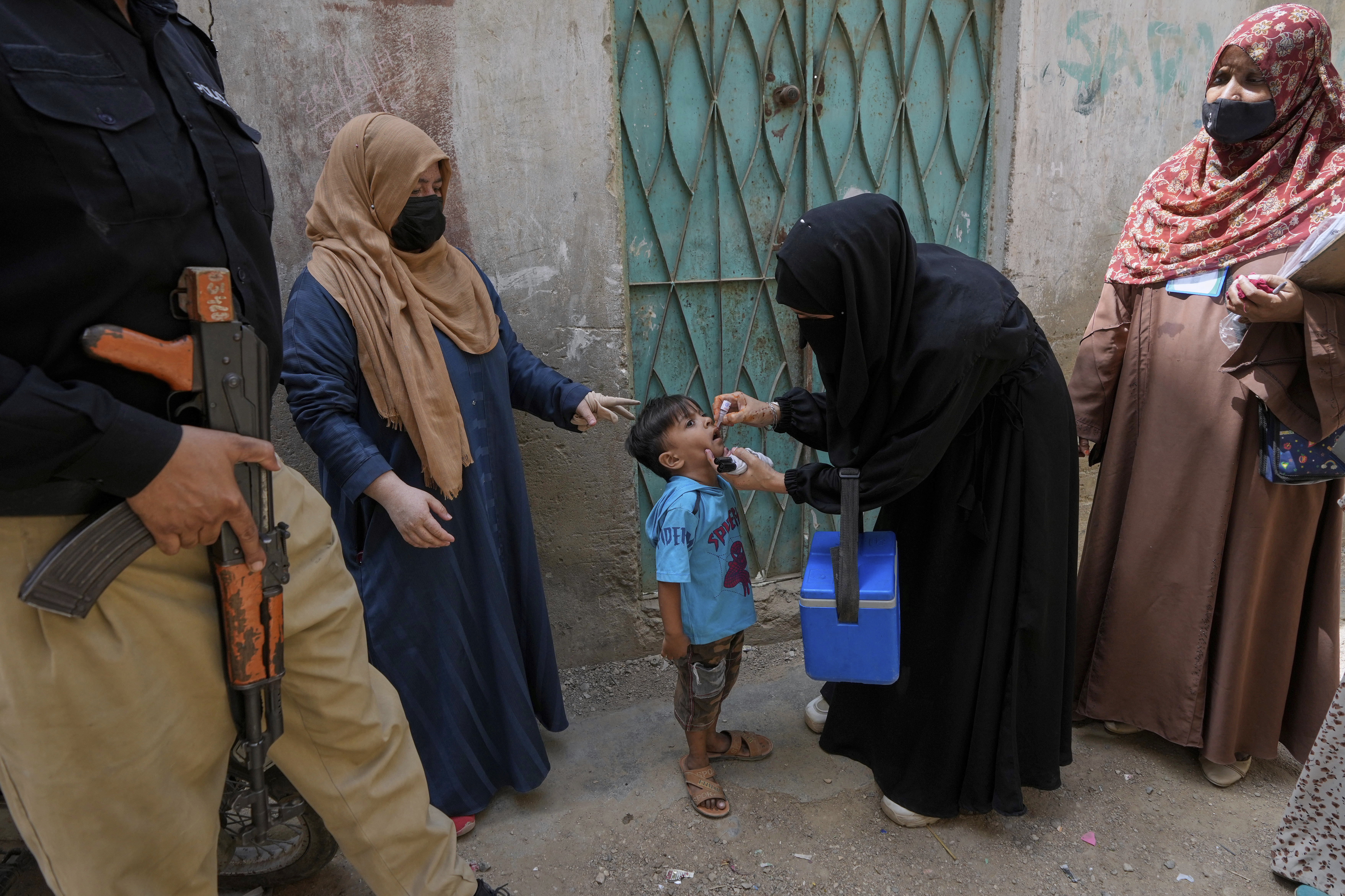 A police officer stands guard while a health worker, center, administers a polio vaccine to a child in Karachi, Pakistan, April 21, 2025. (AP Photo/Fareed Khan)