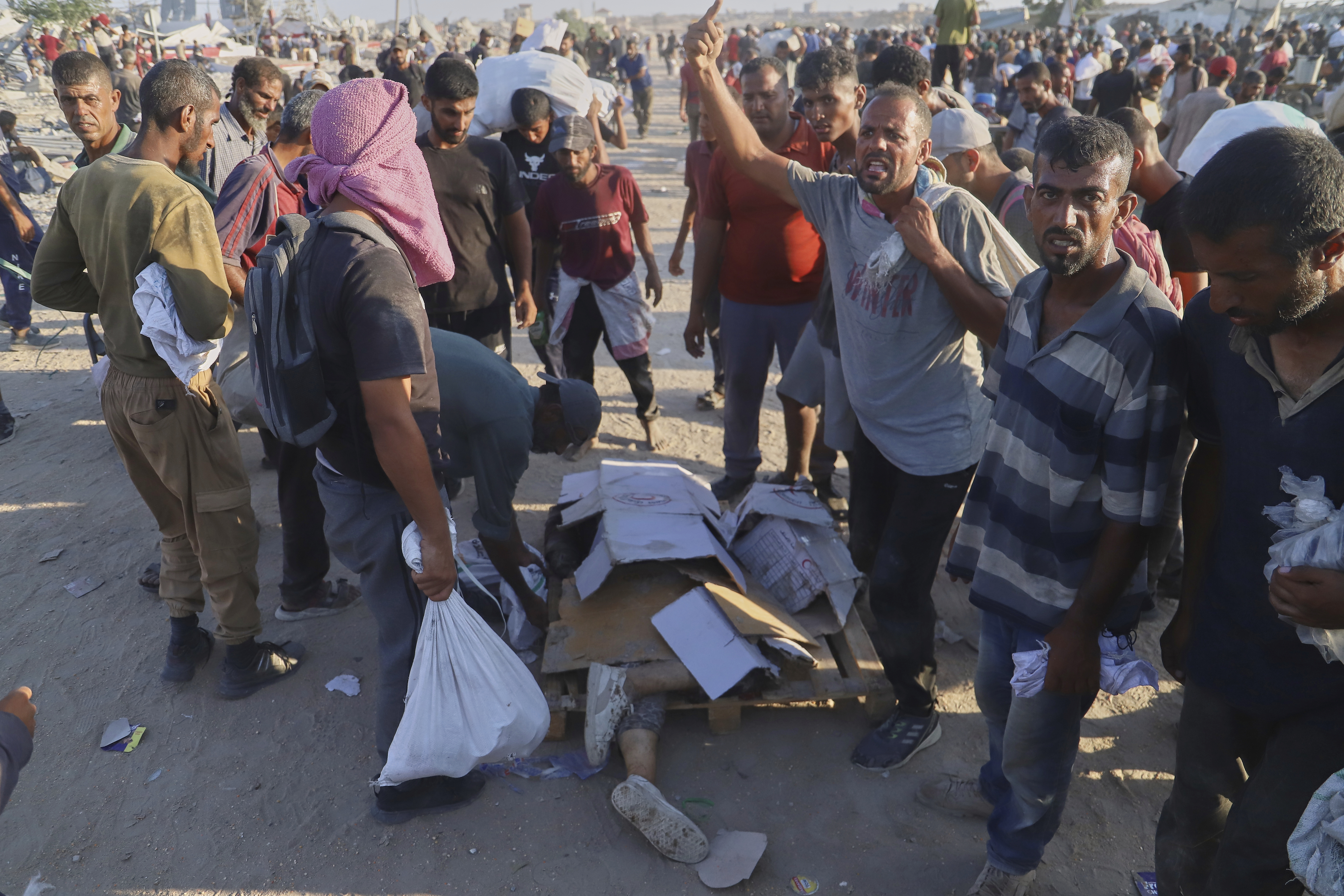Palestinians stand next the body of a woman who was hit by a truck while attempting to reach a humanitarian aid convoy moving along the Morag corridor near Rafah, in the southern Gaza Strip, Monday, Aug. 4, 2025. (AP Photo/Mariam Dagga)