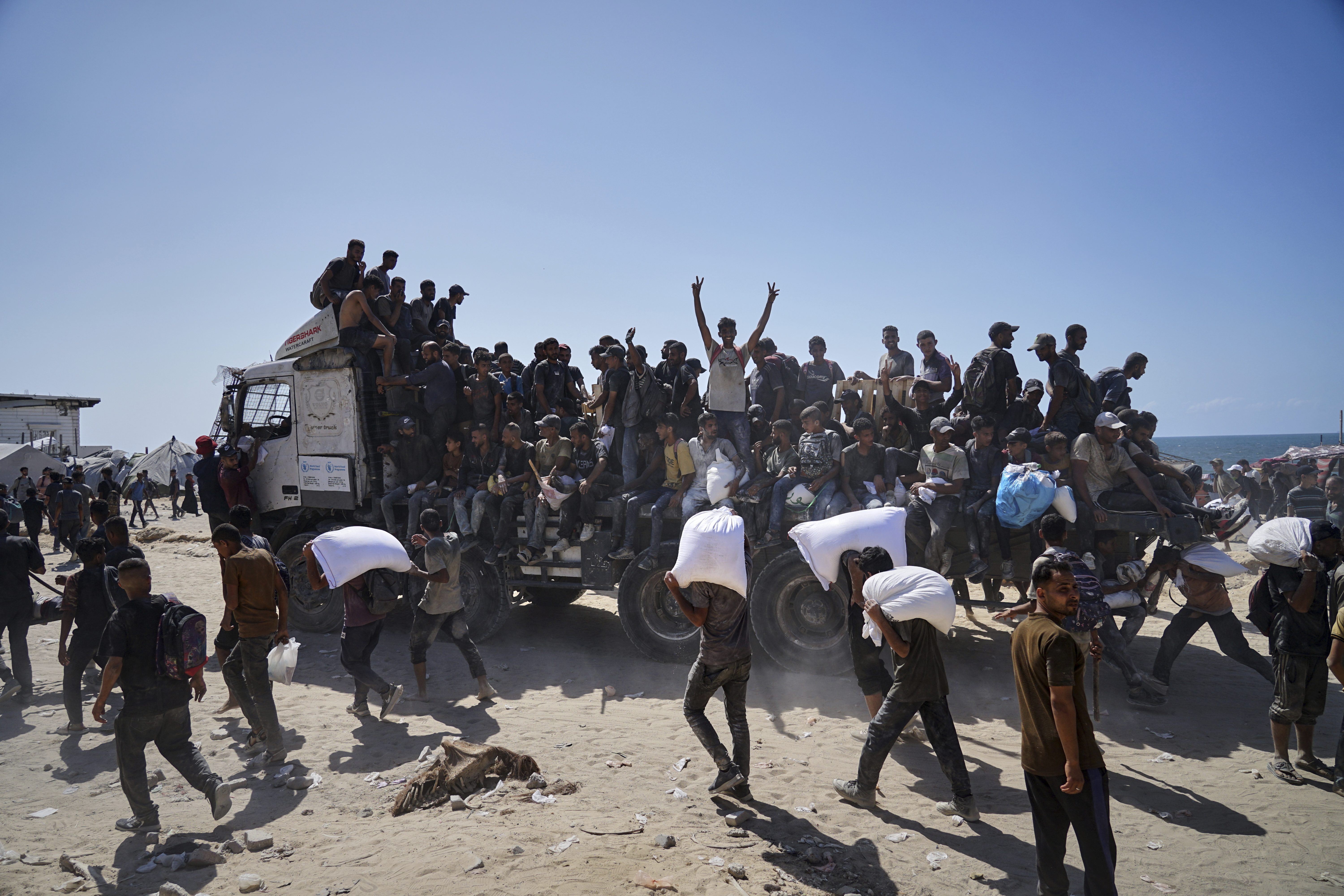 Palestinians carry sacks of flour taken from a humanitarian aid convoy en route to Gaza City, in the outskirts of Beit Lahiya, northern Gaza Strip, Friday, Aug. 1, 2025. (AP Photo/Jehad Alshrafi)