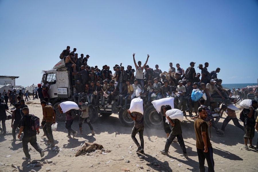Palestinians carry sacks of flour taken from a humanitarian aid convoy en route to Gaza City, in the outskirts of Beit Lahiya, northern Gaza Strip, Friday, Aug. 1, 2025. (AP Photo/Jehad Alshrafi)