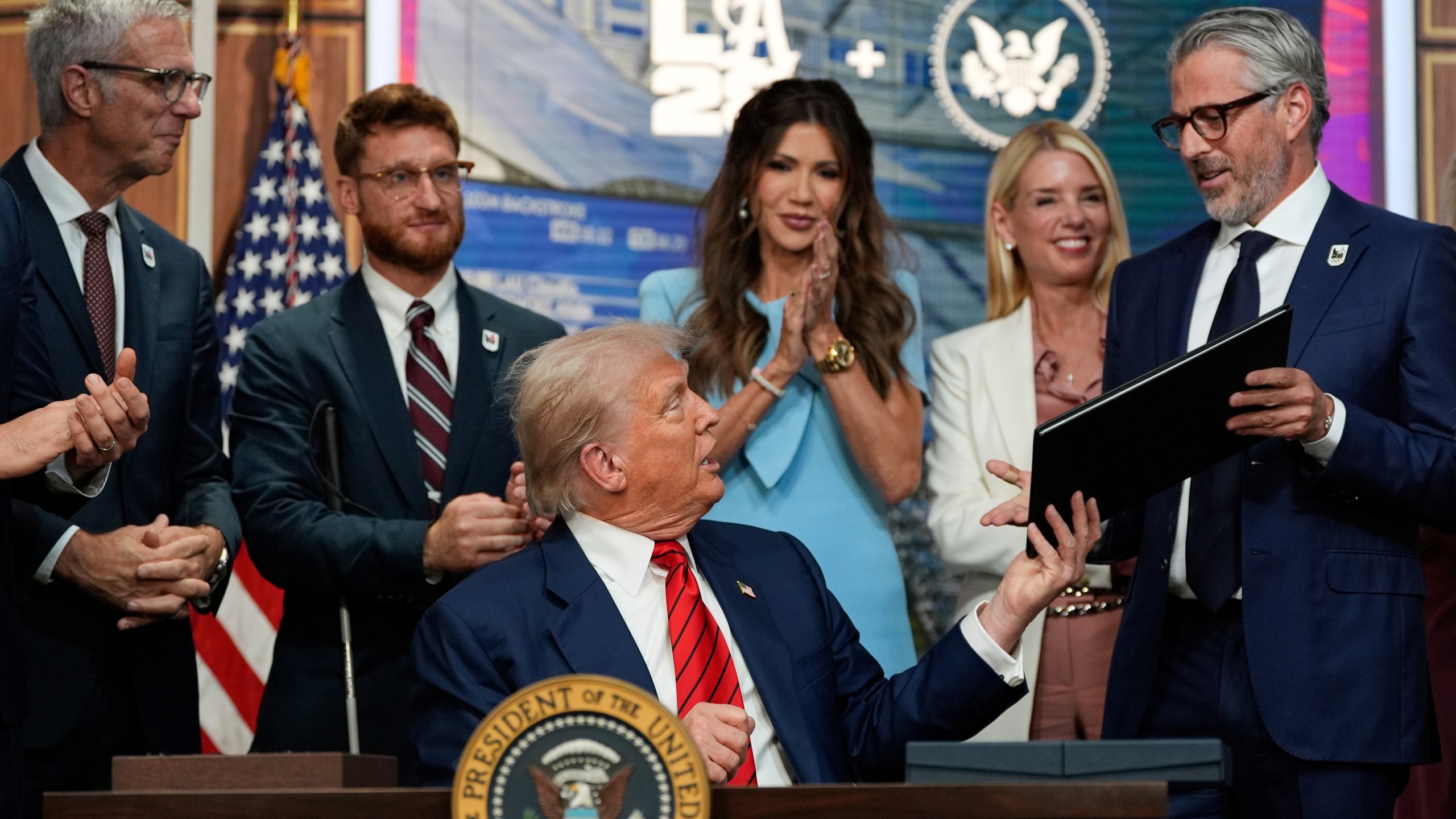 President Donald Trump hands a signed executive order about the 2028 Los Angeles Olympic Games, to Casey Wasserman, chairman of LA28, in the South Court Auditorium of the Eisenhower Executive Office Building on the White House campus, Tuesday, Aug. 5, 2025, in Washington. (AP Photo/Alex Brandon)