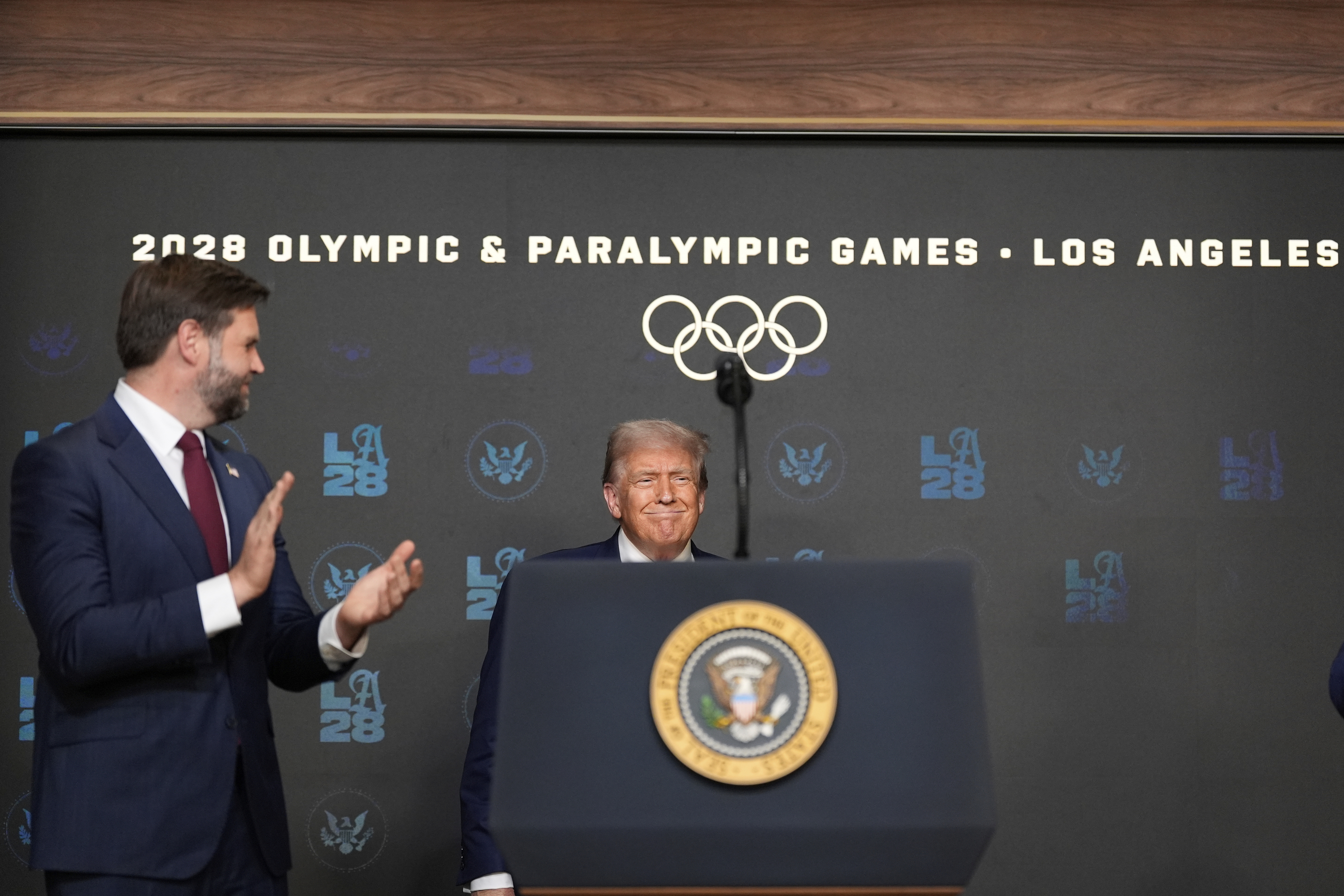 President Donald Trump arrives to speak before signing an executive order about the 2028 Los Angeles Olympic Games, in the South Court Auditorium of the Eisenhower Executive Office Building on the White House campus, Tuesday, Aug. 5, 2025, in Washington, as Vice President JD Vance applauds. (AP Photo/Alex Brandon)