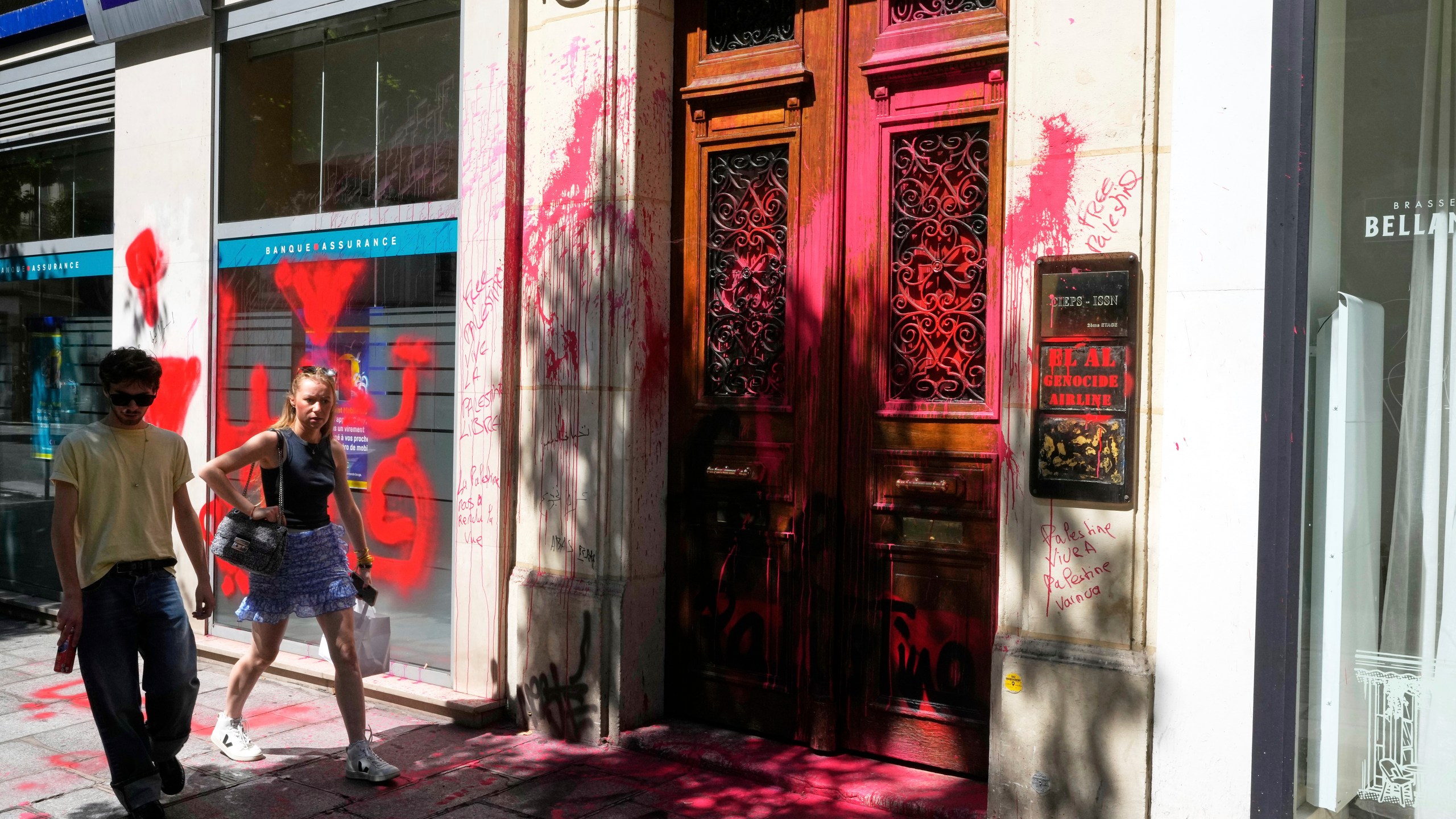People walk by the vandalized Israeli airline El Al Paris office, with anti-Israel graffiti, Thursday, Aug. 7, 2025 in Paris. (AP Photo/Michel Euler)
