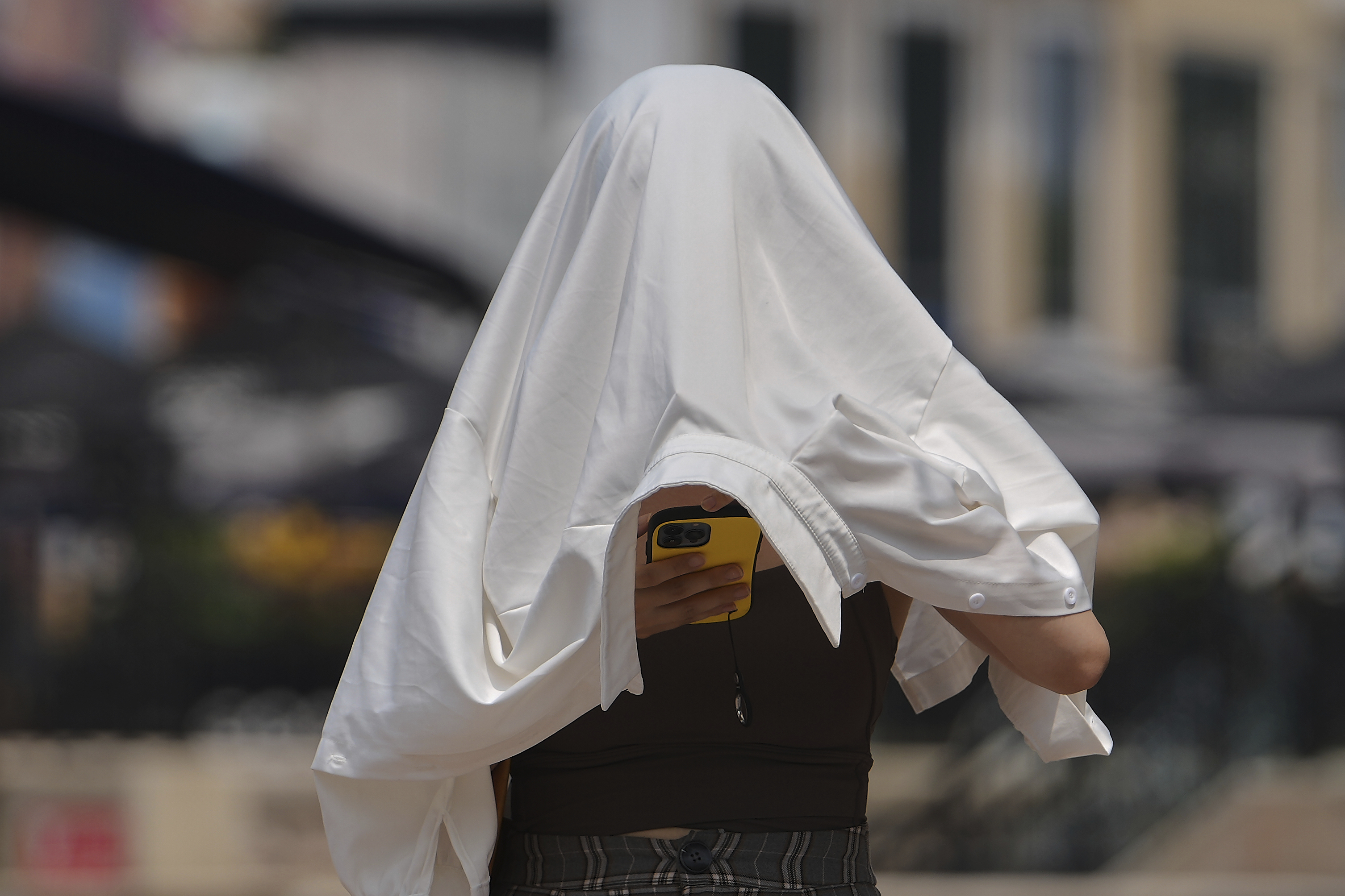 FILE - A woman covers herself from the sun as she browses a smartphone on a street during a hot day in Beijing, Wednesday, July 23, 2025. (AP Photo/Andy Wong, File)