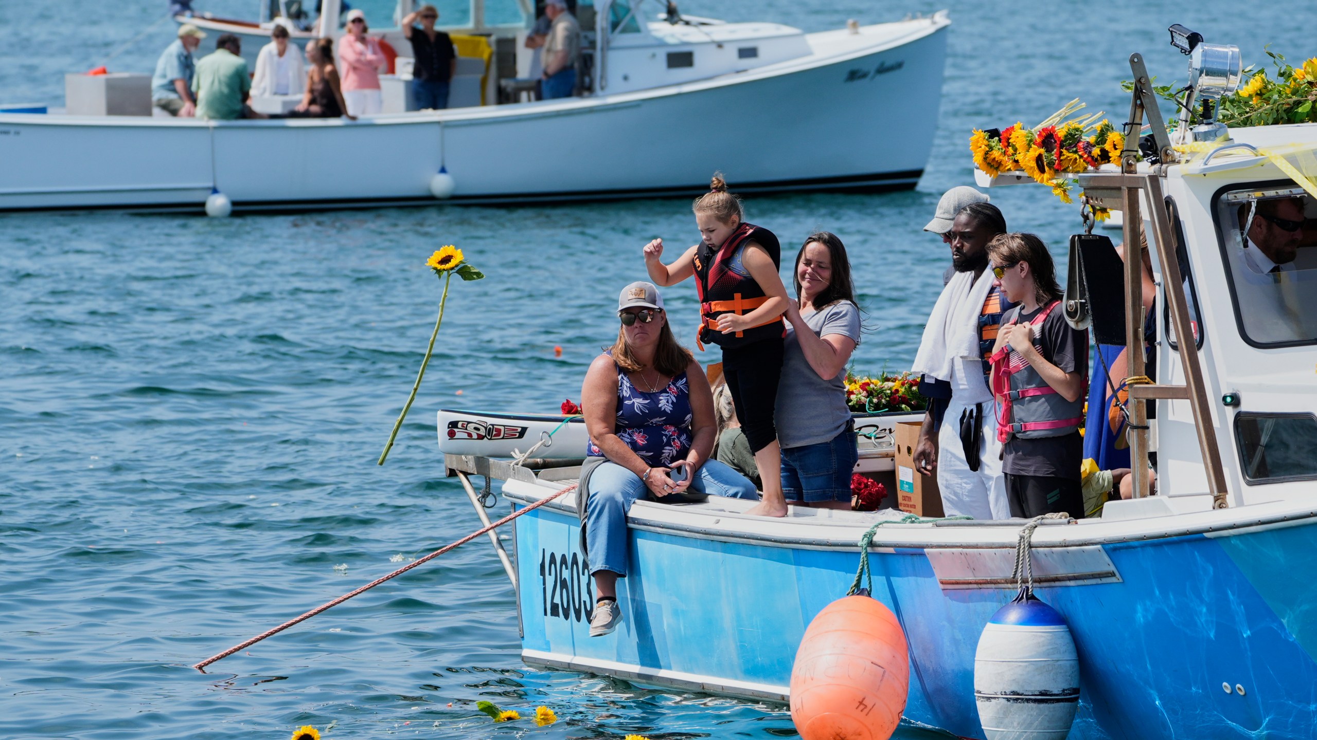 A girl tosses a sunflower into the water in honor of Sunshine Stewart, Sunday, Aug. 10, 2025, in St. George, Maine. (AP Photo/Robert F. Bukaty)
