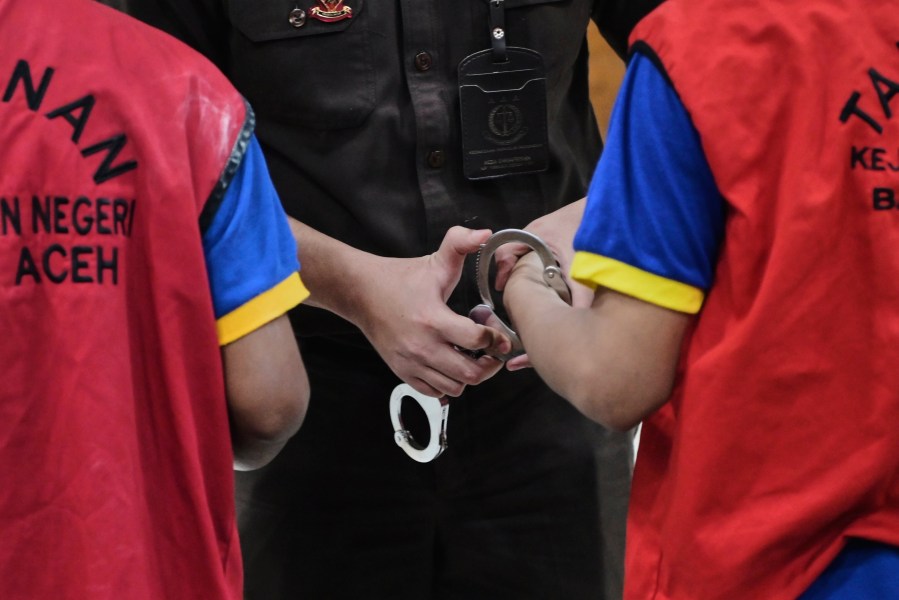 A prosecutor puts a handcuff on two men accused of having gay sex, after their sentencing hearing at a Sharia Court in Banda Aceh, Indonesia, Monday, Aug. 11, 2025. (AP Photo/Reza Saifullah)