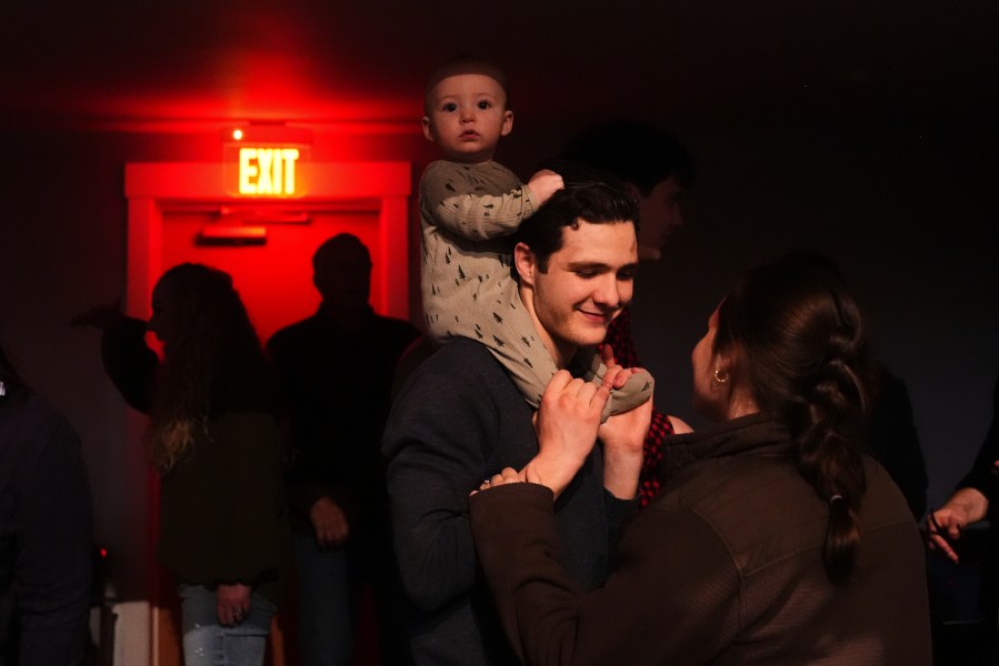Elijah Mooring, whose family attends King's Cross, an offshoot church from Christ Church, holds son Gideon, 9 months, while talking to wife Evangeline as they wait for a performance from Pastor Doug Wilson and the Dads Band, Friday, April 4, 2025, at the Nuart Theatre in Moscow, Idaho. (AP Photo/Lindsey Wasson)