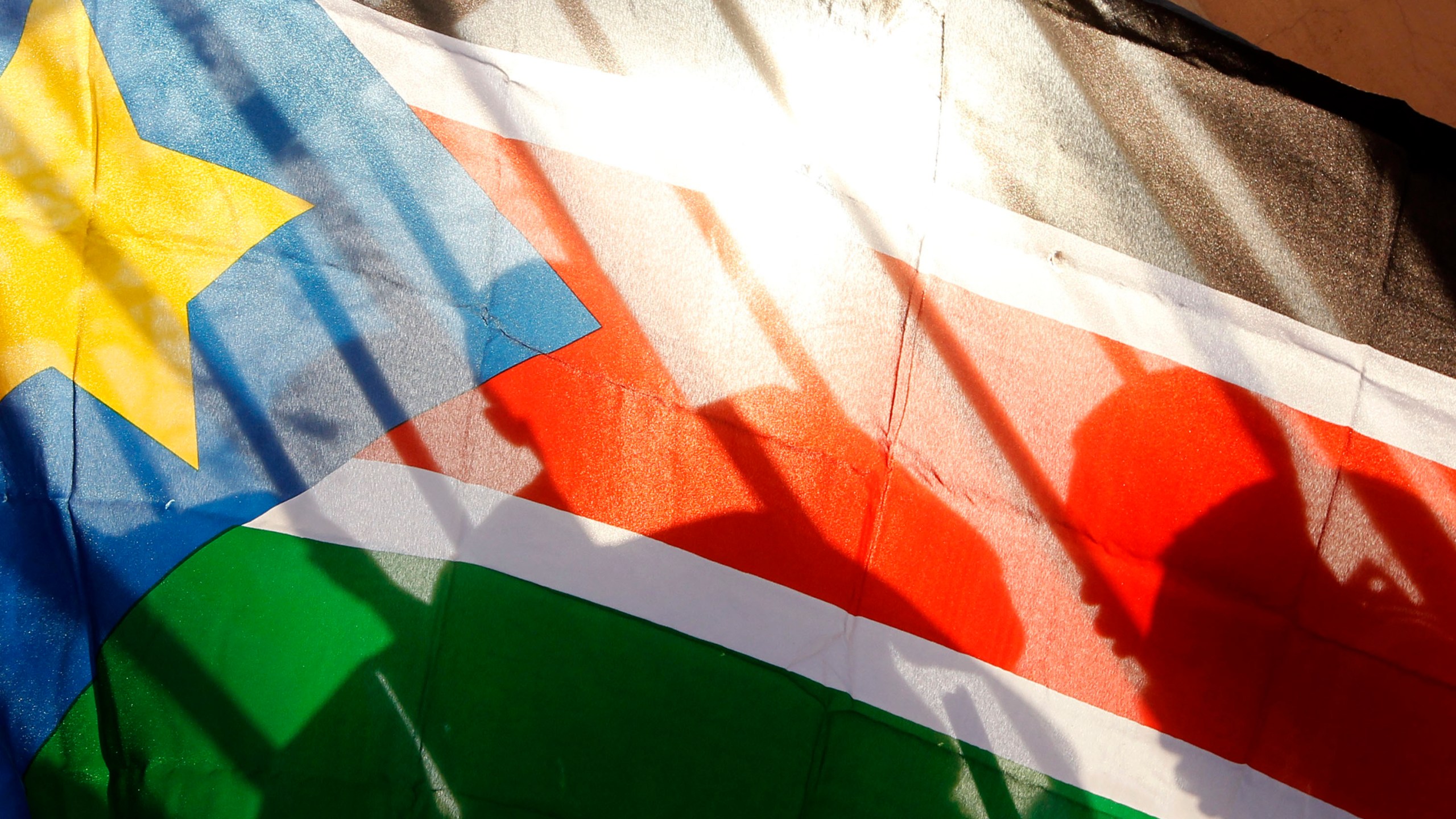 FILE - The silhouettes of South Sudanese people are seen through a South Sudanese flag as they line up to cast their votes in Juba, South Sudan, on Jan. 9, 2011. (AP Photo/Jerome Delay, File)