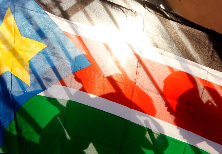 FILE - The silhouettes of South Sudanese people are seen through a South Sudanese flag as they line up to cast their votes in Juba, South Sudan, on Jan. 9, 2011. (AP Photo/Jerome Delay, File)