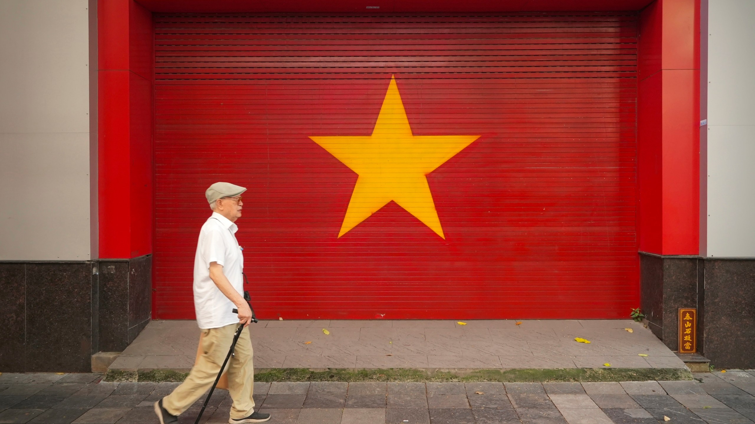 A man walks past a Vietnamese flag painted on a wall in Hanoi, Vietnam on August 12, 2025. (AP Photo/Hau Dinh)
