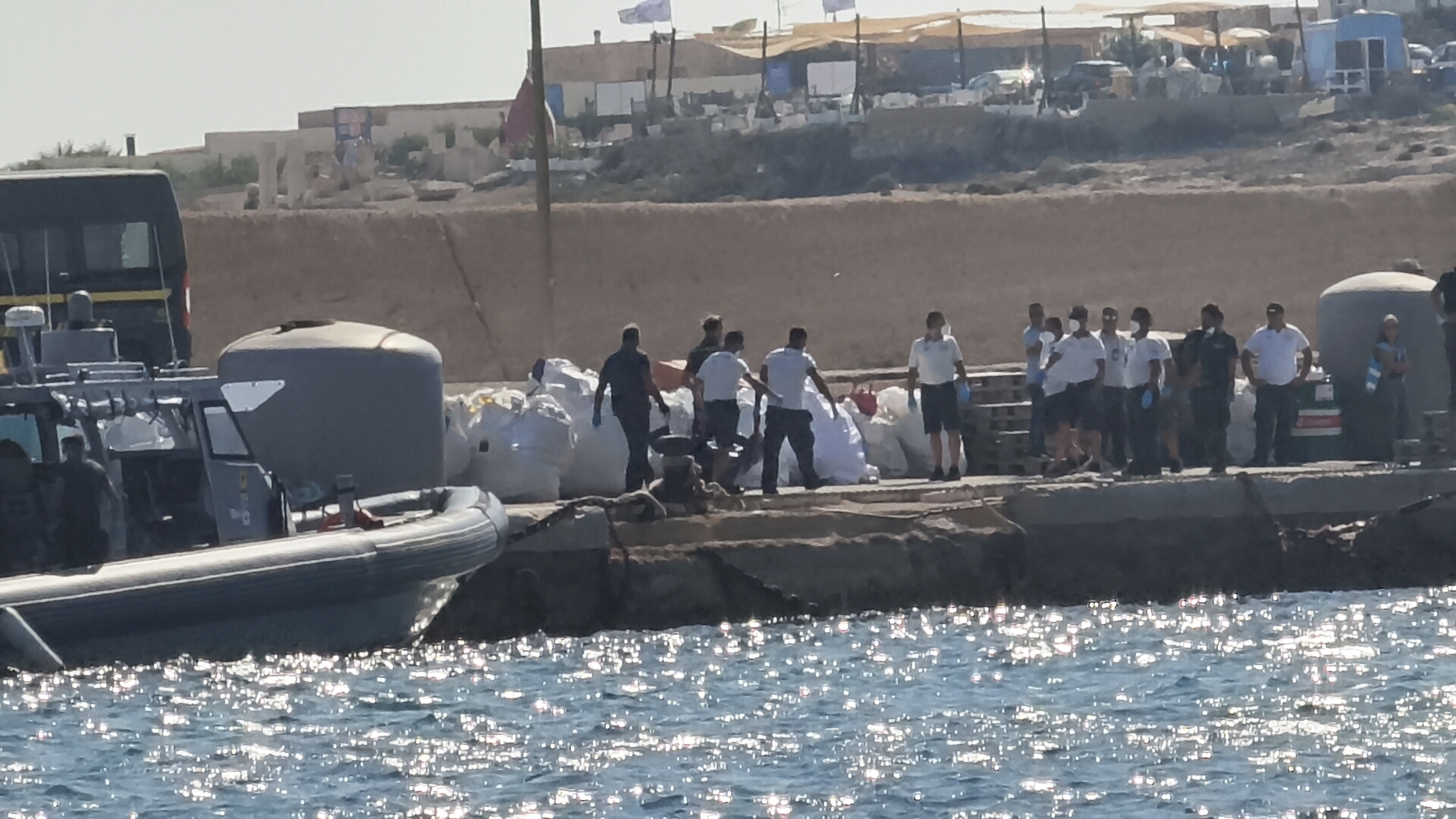 Italian Coast Guards officers carry a body bag on the dock of Lampedusa harbor Wednesday, Aug. 13, 2025, after a boat carrying nearly 100 migrants capsized off the Italian island, killing several people and leaving another dozen missing. (AP Photo/Elio Deisderio)