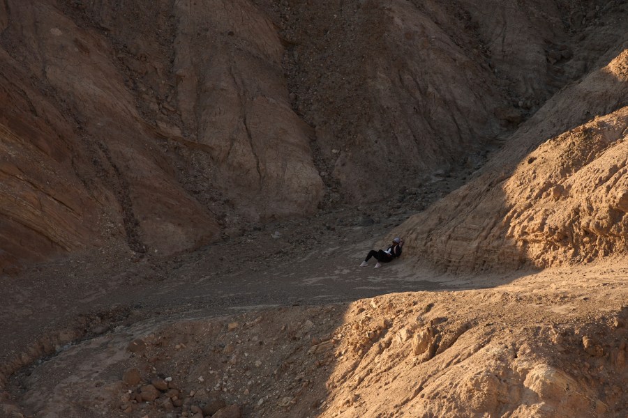 A hiker rests in the shade near Zabriskie Point, Sunday, Aug. 3, 2025, in Death Valley National Park, Calif. (AP Photo/John Locher)