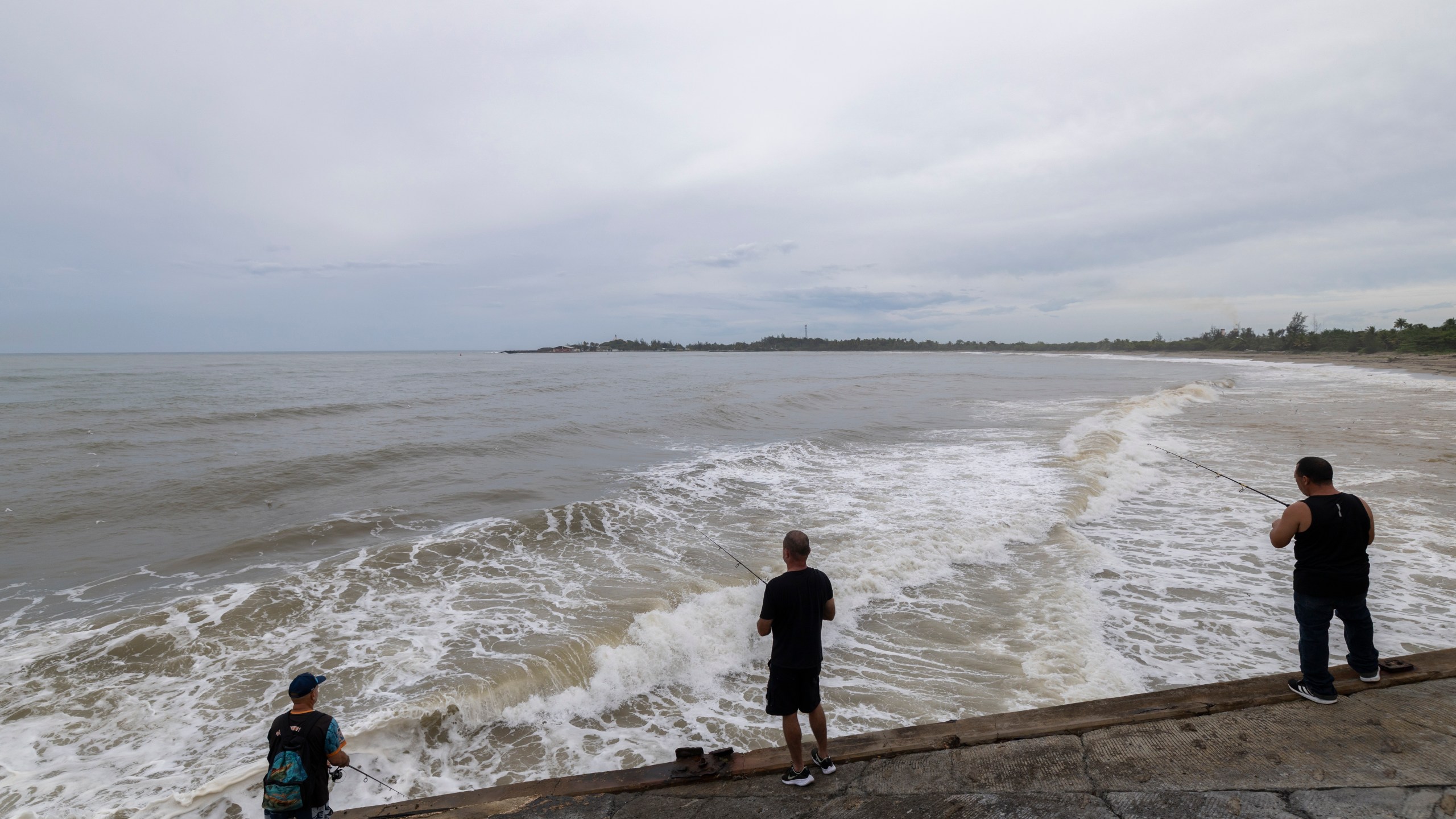 People fish along the shore in Arecibo, Puerto Rico, as Hurricane Erin brings rains to the island, Sunday, Aug. 17, 2025. (AP Photo/Alejandro Granadillo)
