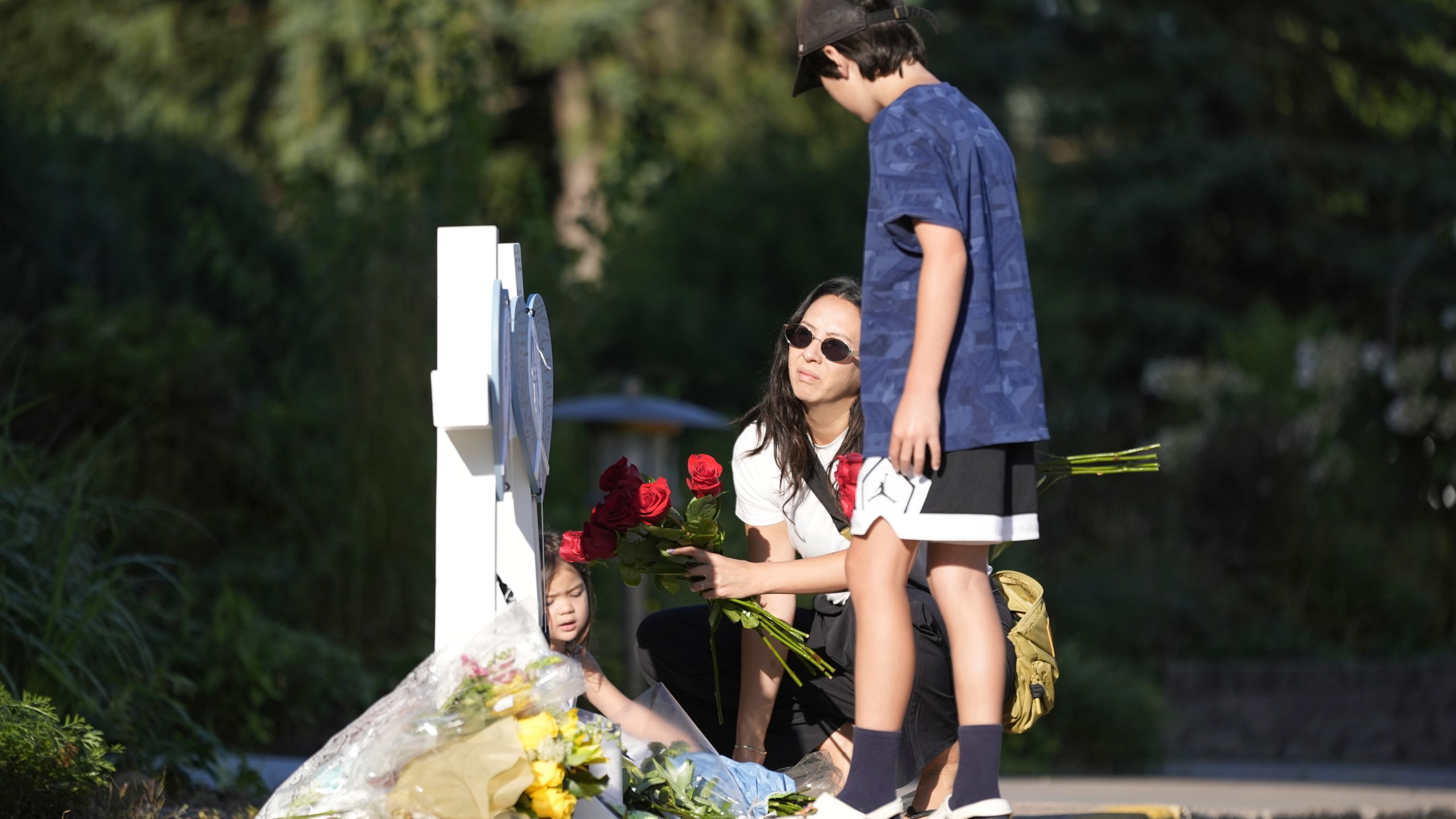 Amy Dols, and her children, Archie and Paloma place flowers at a memorial at Annunciation Catholic Church after Wednesday's school shooting, Thursday, Aug. 28, 2025, in Minneapolis. (AP Photo/Abbie Parr)