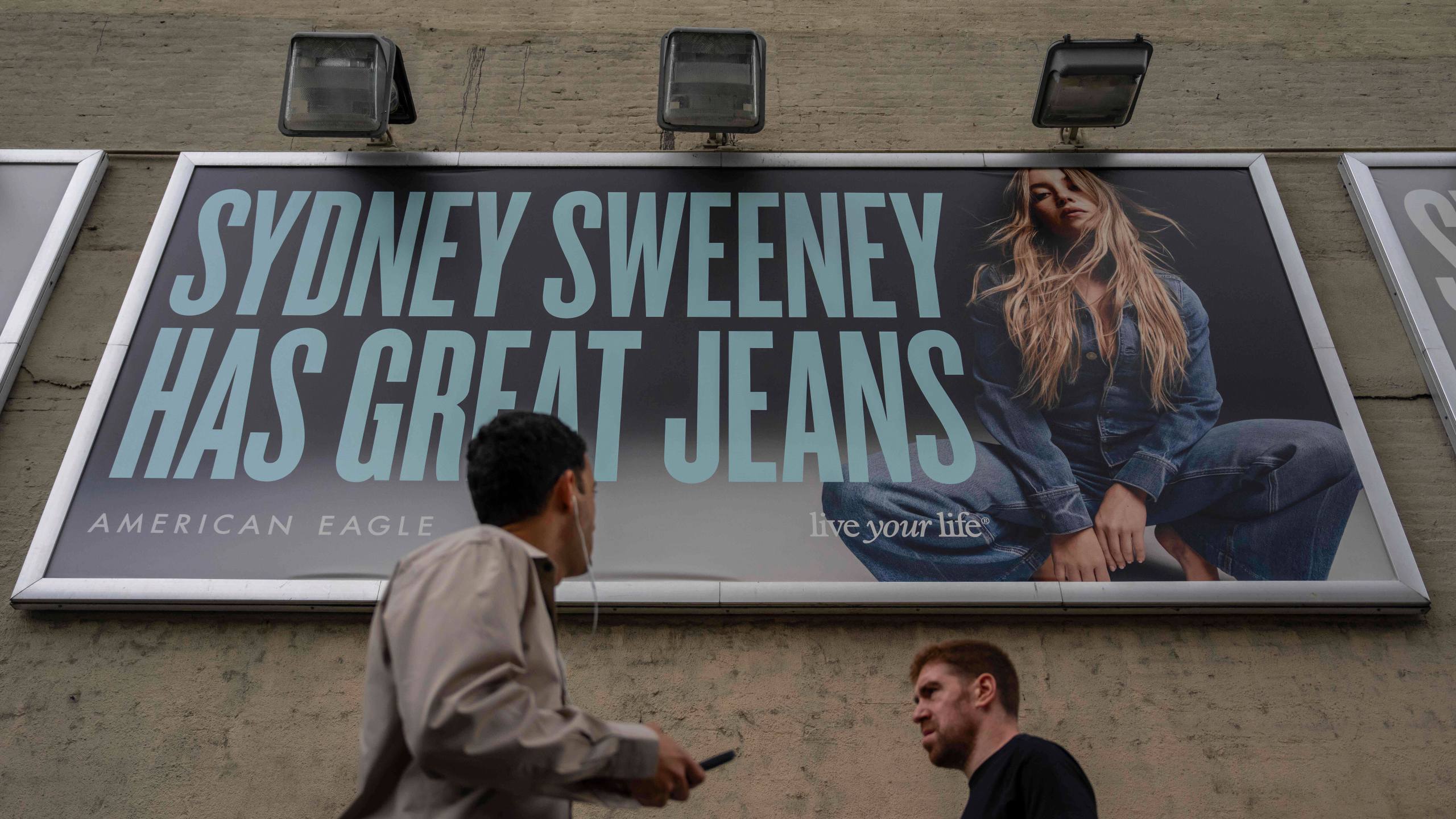 FILE - People walk past a campaign poster starring Sydney Sweeney which is displayed at the American Eagle Outfitters store, Friday, Aug. 1, 2025, in New York. (AP Photo/Yuki Iwamura, File)