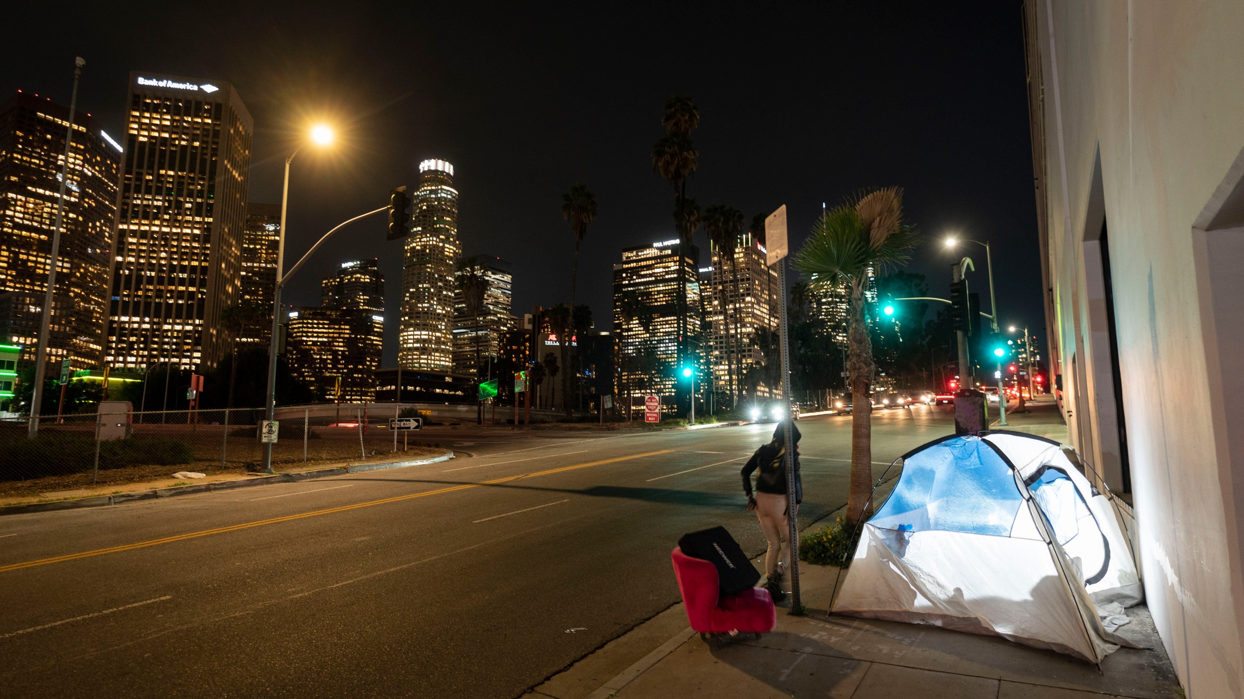 FILE - In this photo illuminated by an off-camera flash, a woman walks past a homeless person's tent with a chair in downtown Los Angeles, Feb. 16, 2023. (AP Photo/Jae C. Hong, File)