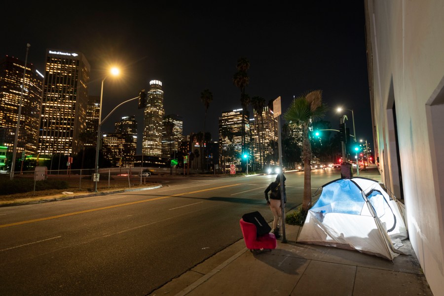 FILE - In this photo illuminated by an off-camera flash, a woman walks past a homeless person's tent with a chair in downtown Los Angeles, Feb. 16, 2023. (AP Photo/Jae C. Hong, File)