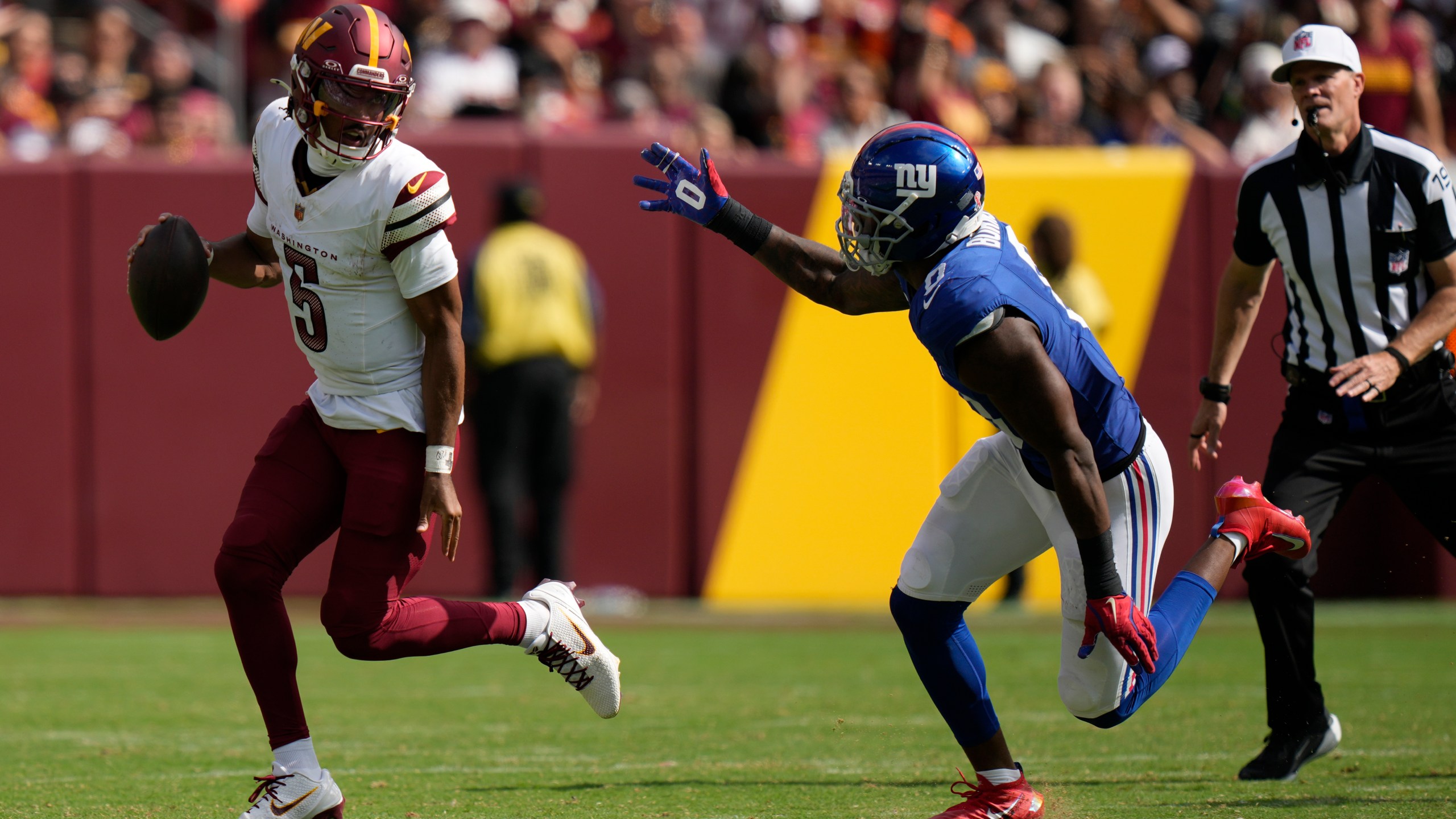 Washington Commanders quarterback Jayden Daniels (5) is chased by New York Giants linebacker Brian Burns (0) during the second half of an NFL football game, Sunday, Sept. 7, 2025, in Landover, Md. (AP Photo/Stephanie Scarbrough)