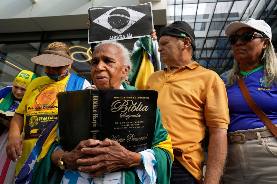 A supporter holding a Bible waits for the arrival of former President Jair Bolsonaro at a hospital, after he was temporarily allowed out of house arrest for medical treatment, in Brasilia, Brazil, Sunday, Sep. 14, 2025. (AP Photo/Eraldo Peres)