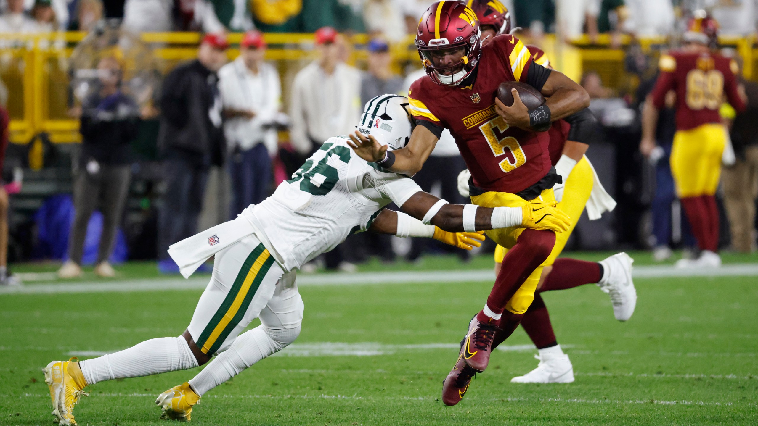 Washington Commanders quarterback Jayden Daniels (5) runs with the ball as Green Bay Packers linebacker Edgerrin Cooper (56) defends during the first half of an NFL football game Thursday, Sept. 11, 2025, in Green Bay, Wis. (AP Photo/Mike Roemer)