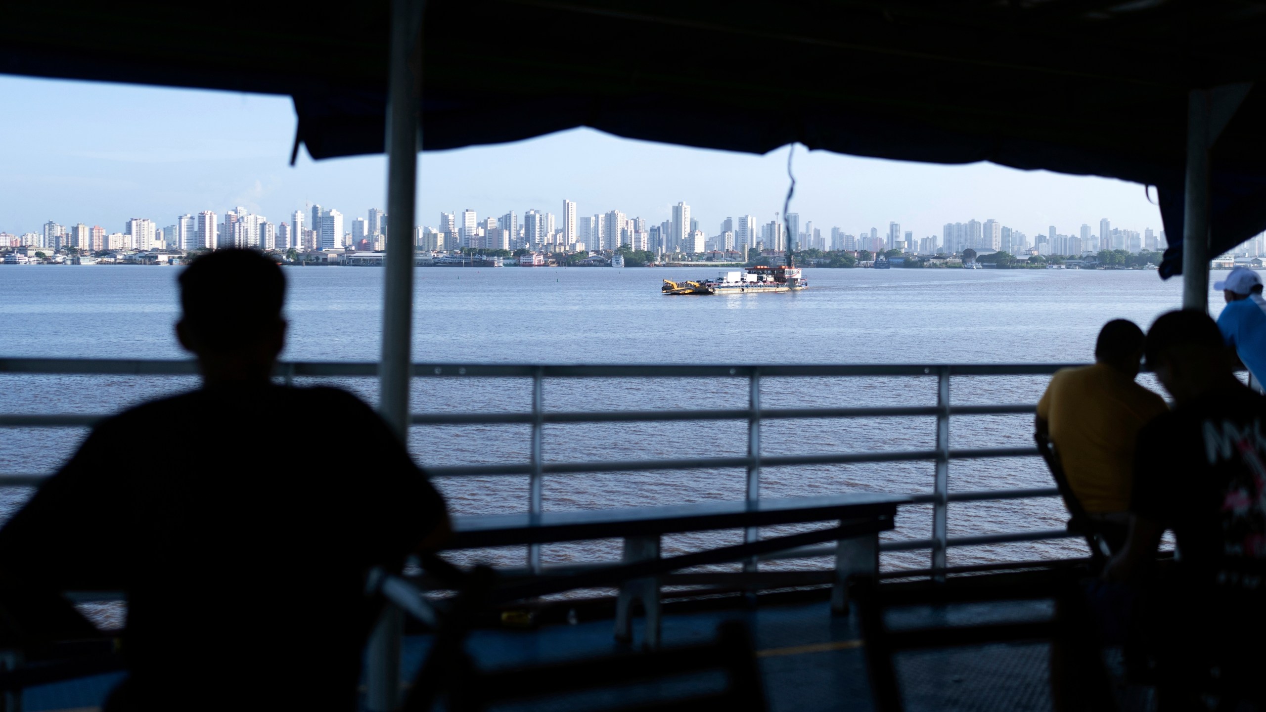 FILE - People look out at the coast of Belem, Brazil, as a boat nears shore, March 23, 2025. (AP Photo/Jorge Saenz, File)