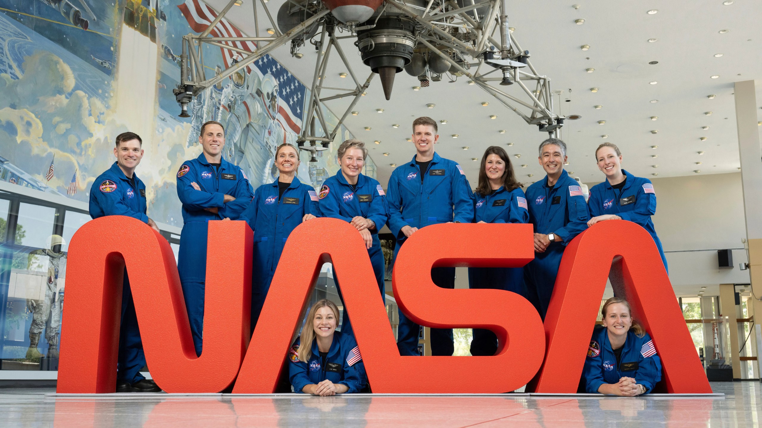In this undated photo released by NASA, NASA's 10 newest astronauts pose behind the logo at at NASA’s Johnson Space Center in Houston, Texas. Left to right; Sept. 22, 2025. The 10 candidates, pictured here at NASA’s Johnson Space Center in Houston. U.S. Army CW3 Ben Bailey, U.S. Air Force Maj. Cameron Jones, Katherine Spies, Anna Menon, U.S. Navy Lt. Cmdr. Erin Overcash, U.S. Air Force Maj. Adam Fuhrmann, Lauren Edgar, Yuri Kubo, Rebecca Lawler, and Dr. Imelda Muller. (NASA via AP)