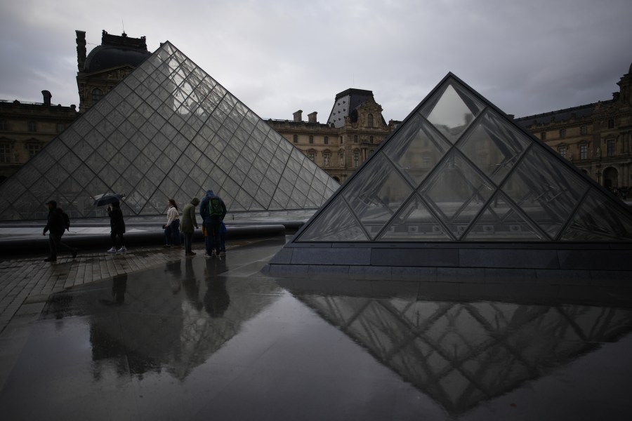People tour the courtyard of Le Louvre museum in the rain Monday, Oct. 27, 2025 in Paris. (AP Photo/Christophe Ena)