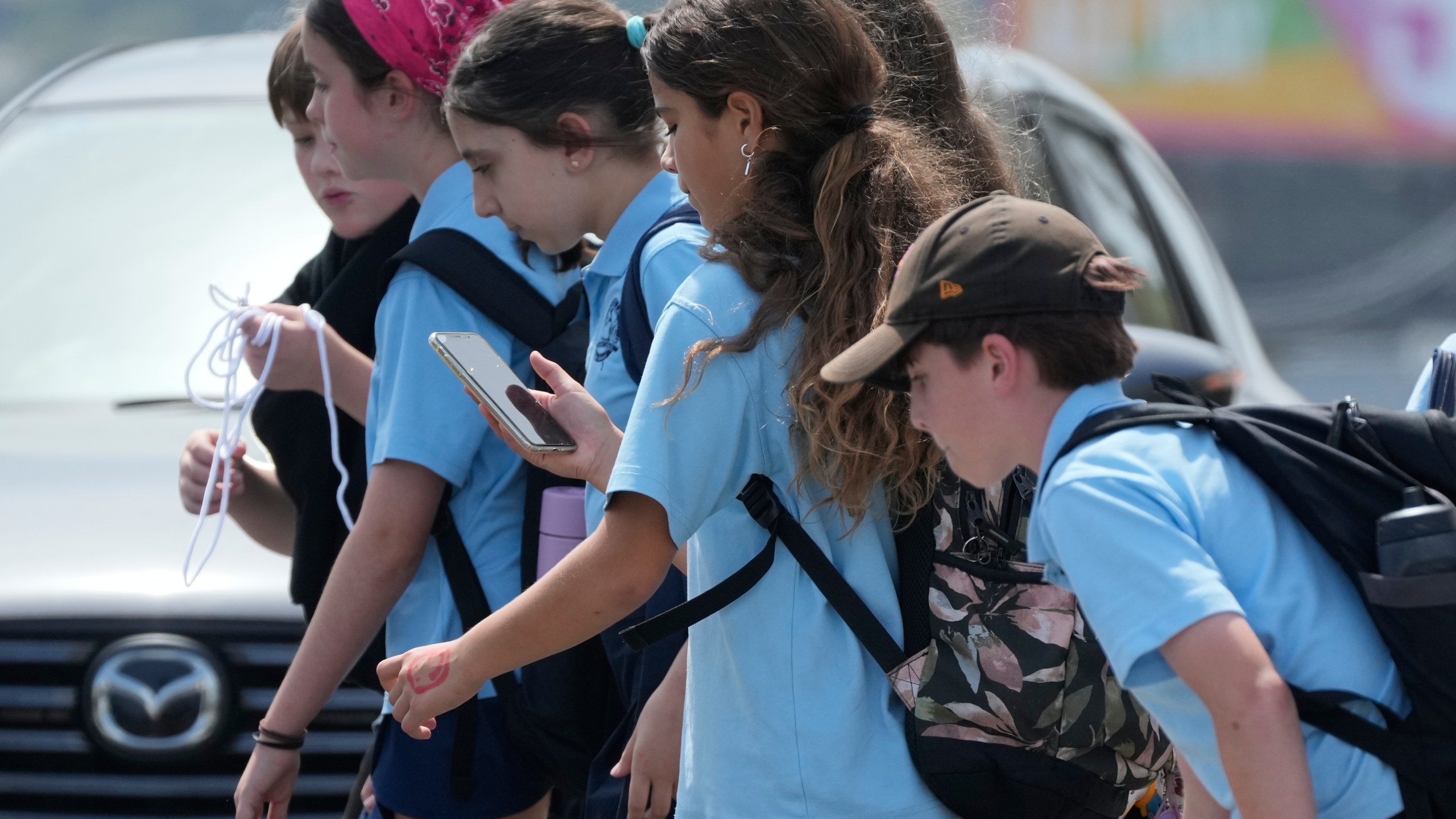 A school girl uses her phone as she walks with a group of kids in Sydney, Monday, Dec. 8, 2025. (AP Photo/Rick Rycroft)