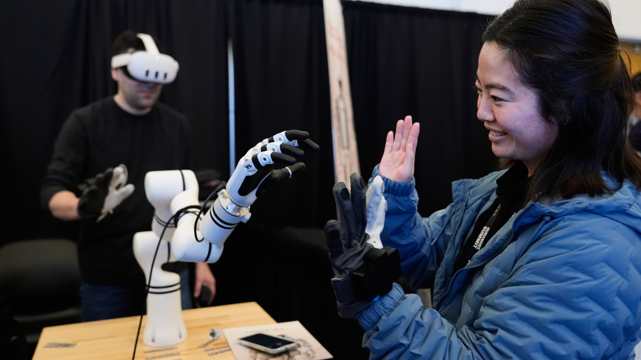 Yuka Iwashita, right, interacts with a robotic hand at the Alt-Bionics table during the Humanoids Summit, Thursday, Dec. 11, 2025, in Mountain View, Calif. (AP Photo/Godofredo A. Vásquez)