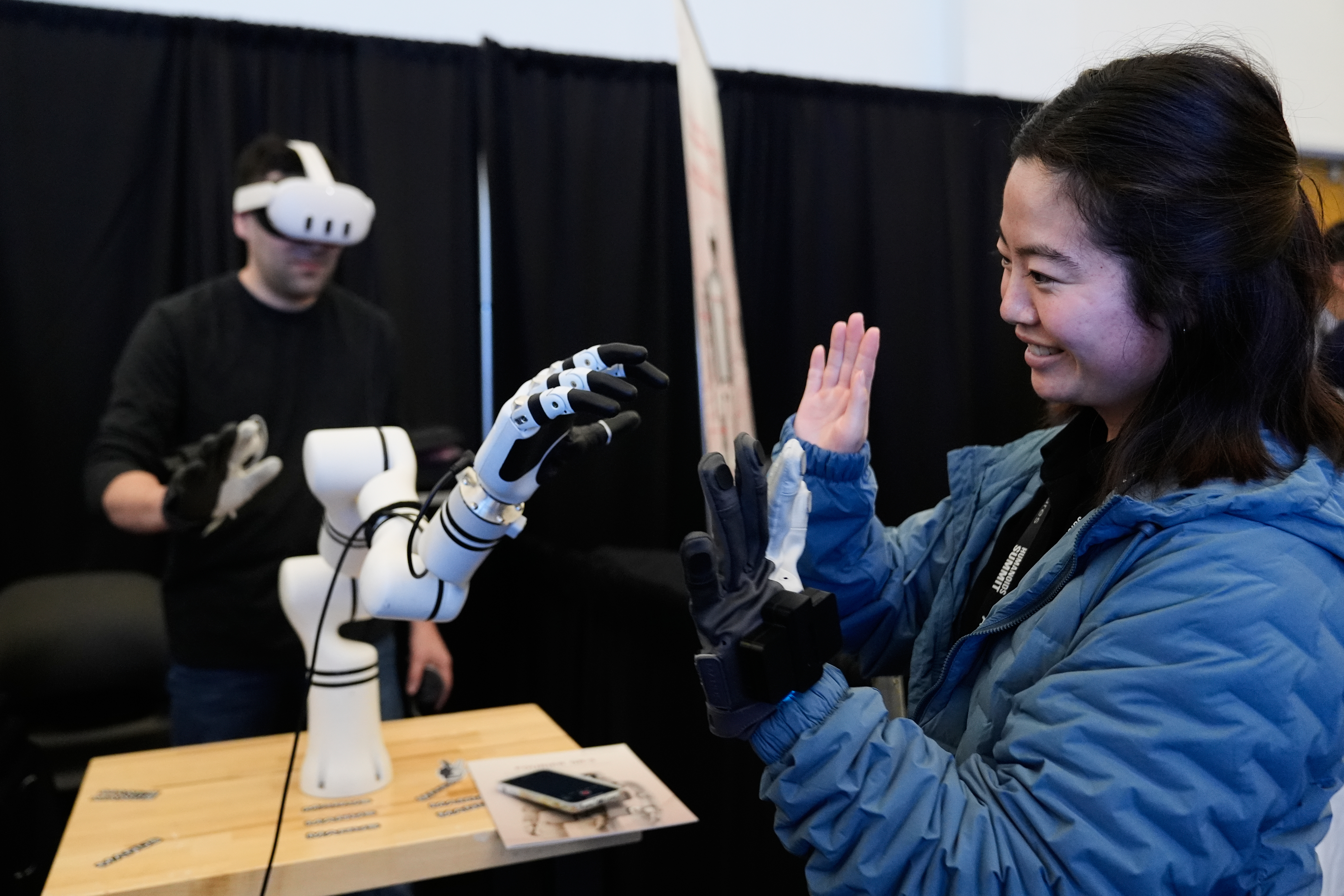 Yuka Iwashita, right, interacts with a robotic hand at the Alt-Bionics table during the Humanoids Summit, Thursday, Dec. 11, 2025, in Mountain View, Calif. (AP Photo/Godofredo A. Vásquez)