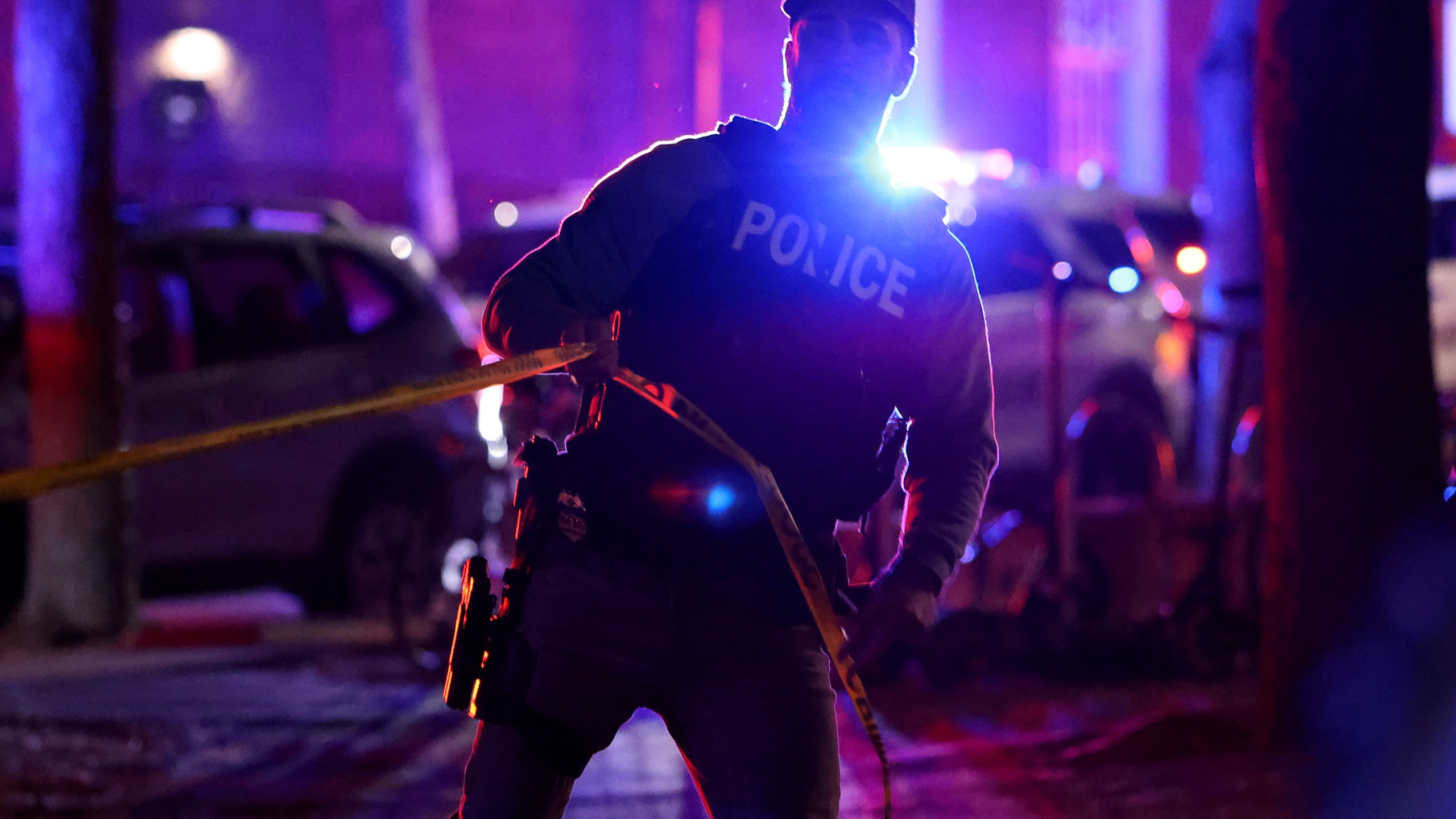 A police officer hangs yellow crime tape at Brown University in Providence, R.I., on Saturday, Dec. 13, 2025, during the investigation of a shooting. (AP Photo/Mark Stockwell)