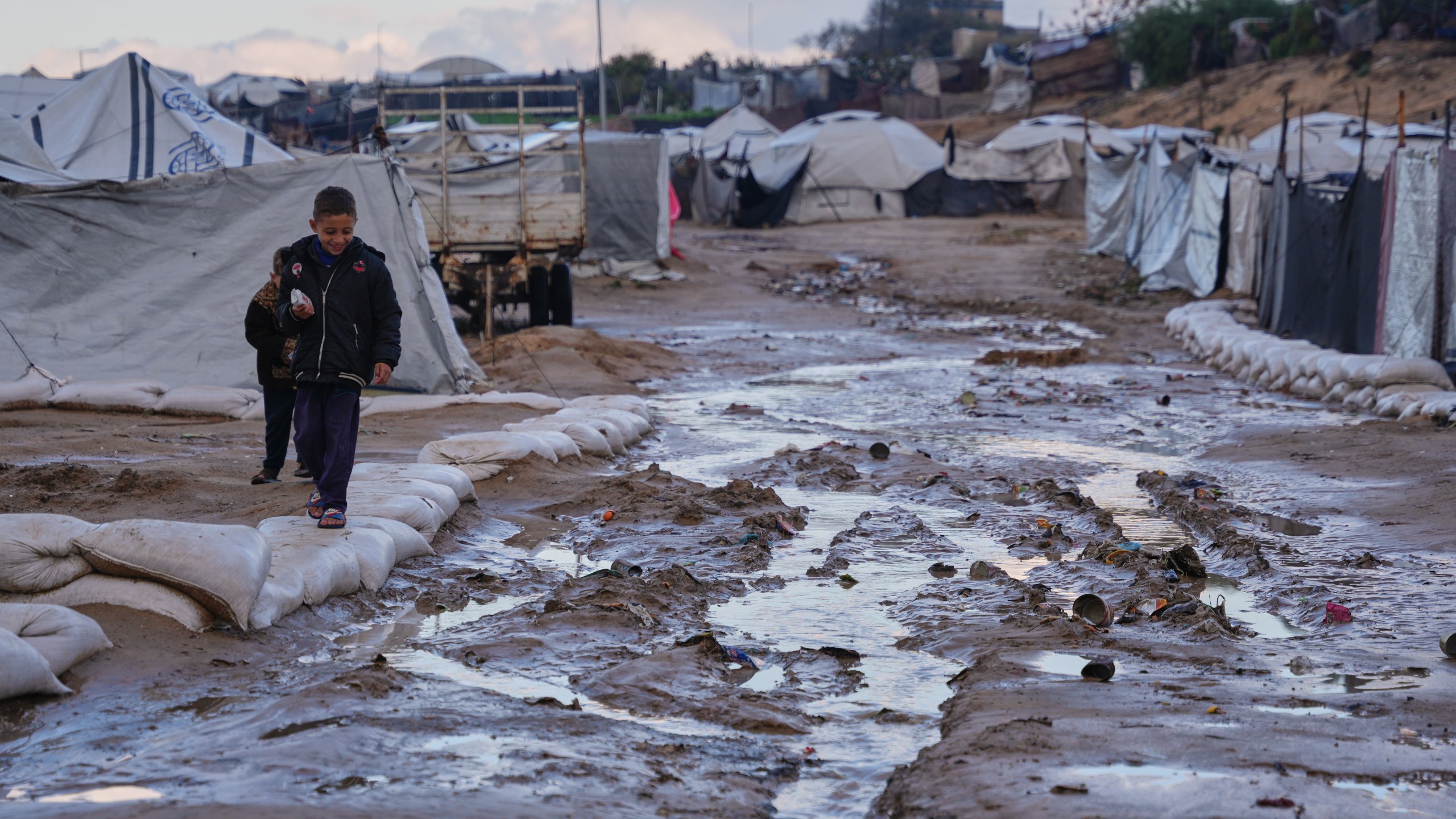 Palestinian children walk past mud puddle after heavy rains in a makeshift camp for displaced people in Zawaida, central Gaza Strip, Wednesday, Dec. 17, 2025. (AP Photo/Abdel Kareem Hana)